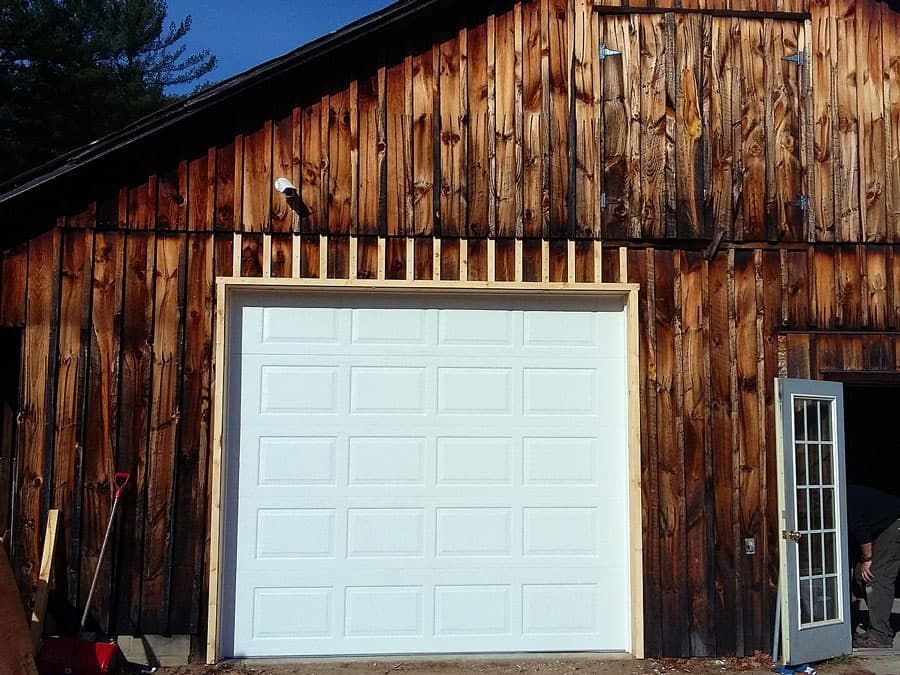 A white garage door in front of a wooden building