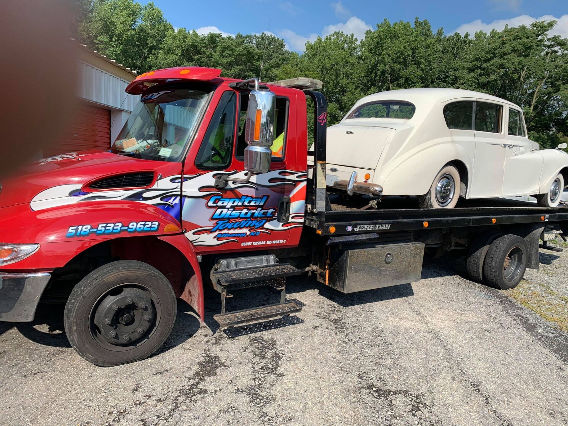A red tow truck is towing a white car.