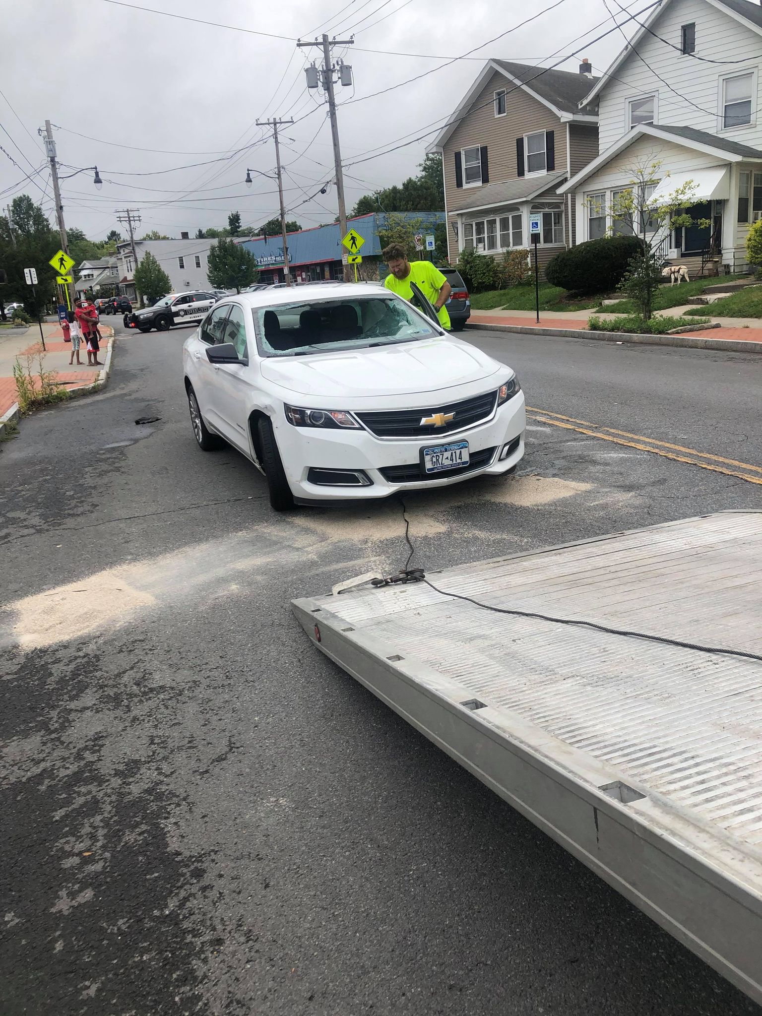 A white car is driving down a street next to a tow truck.
