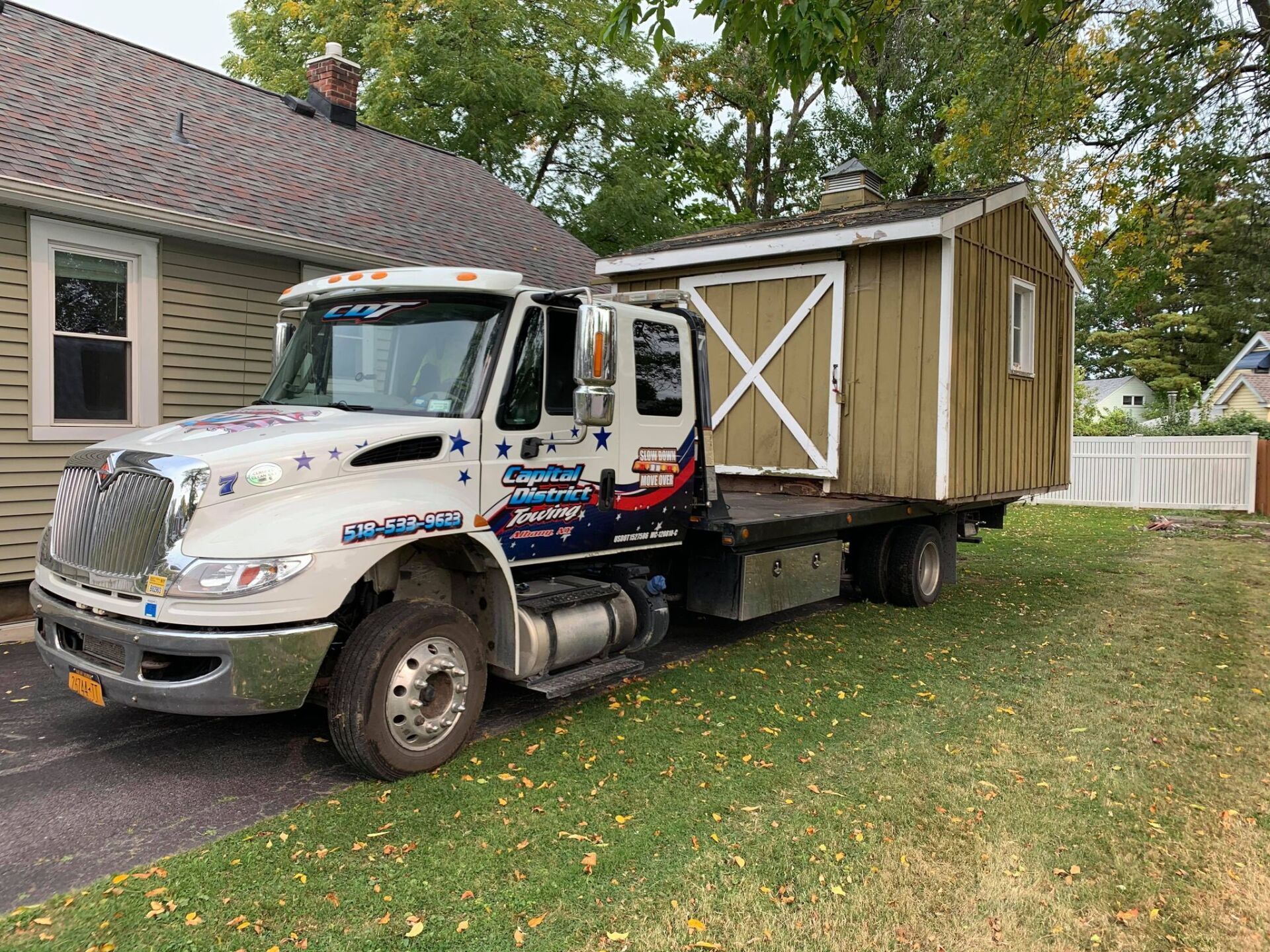 A tow truck is carrying a shed to a house.