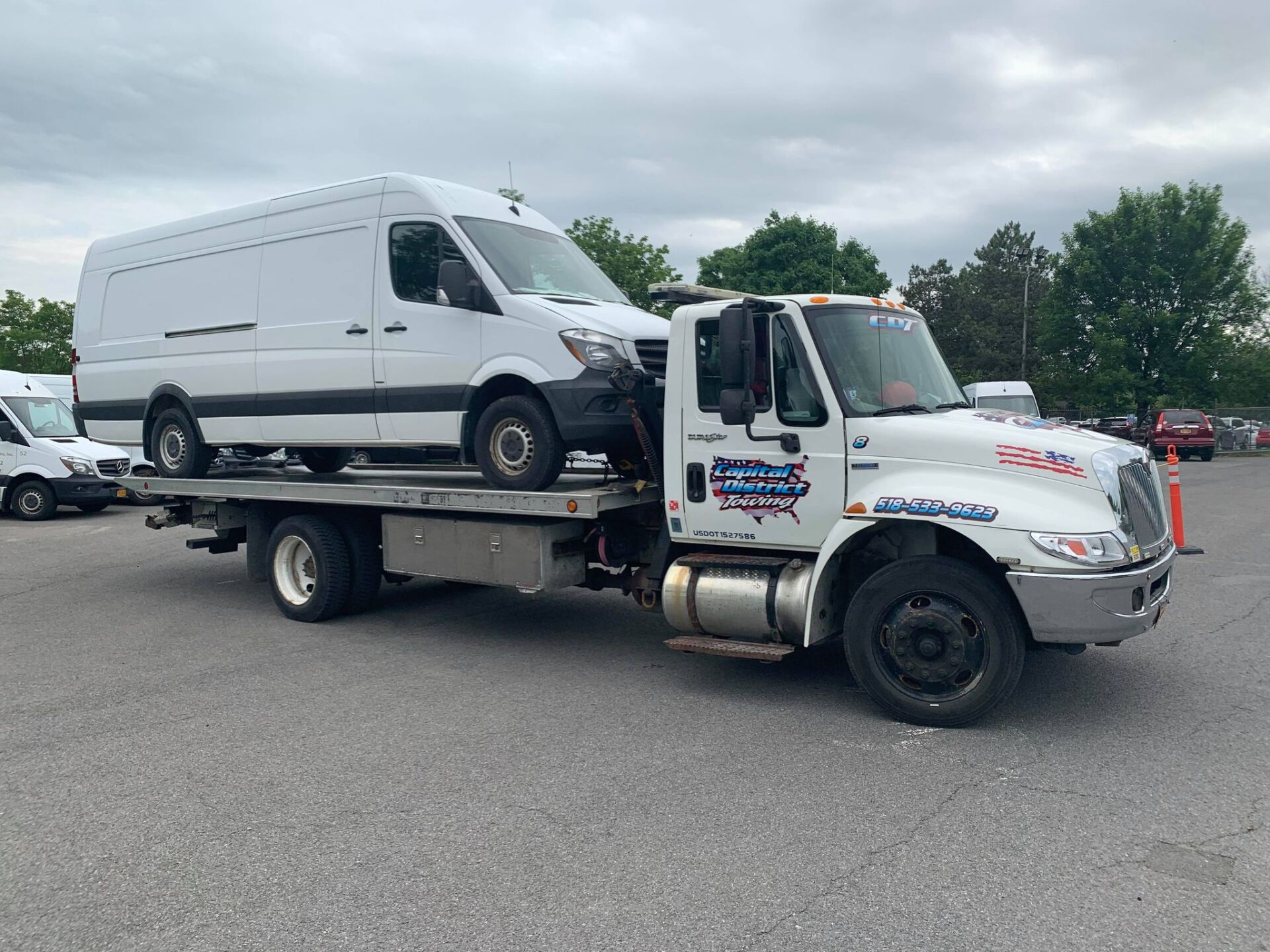 A tow truck is towing a white van in a parking lot.