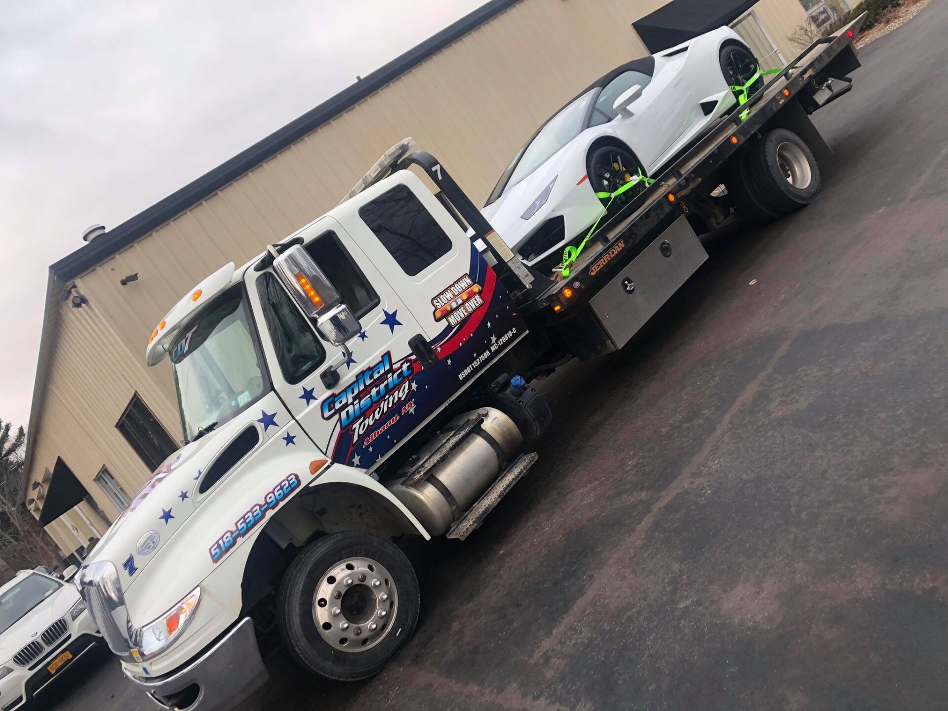 A white tow truck is carrying a white car on the back of it.