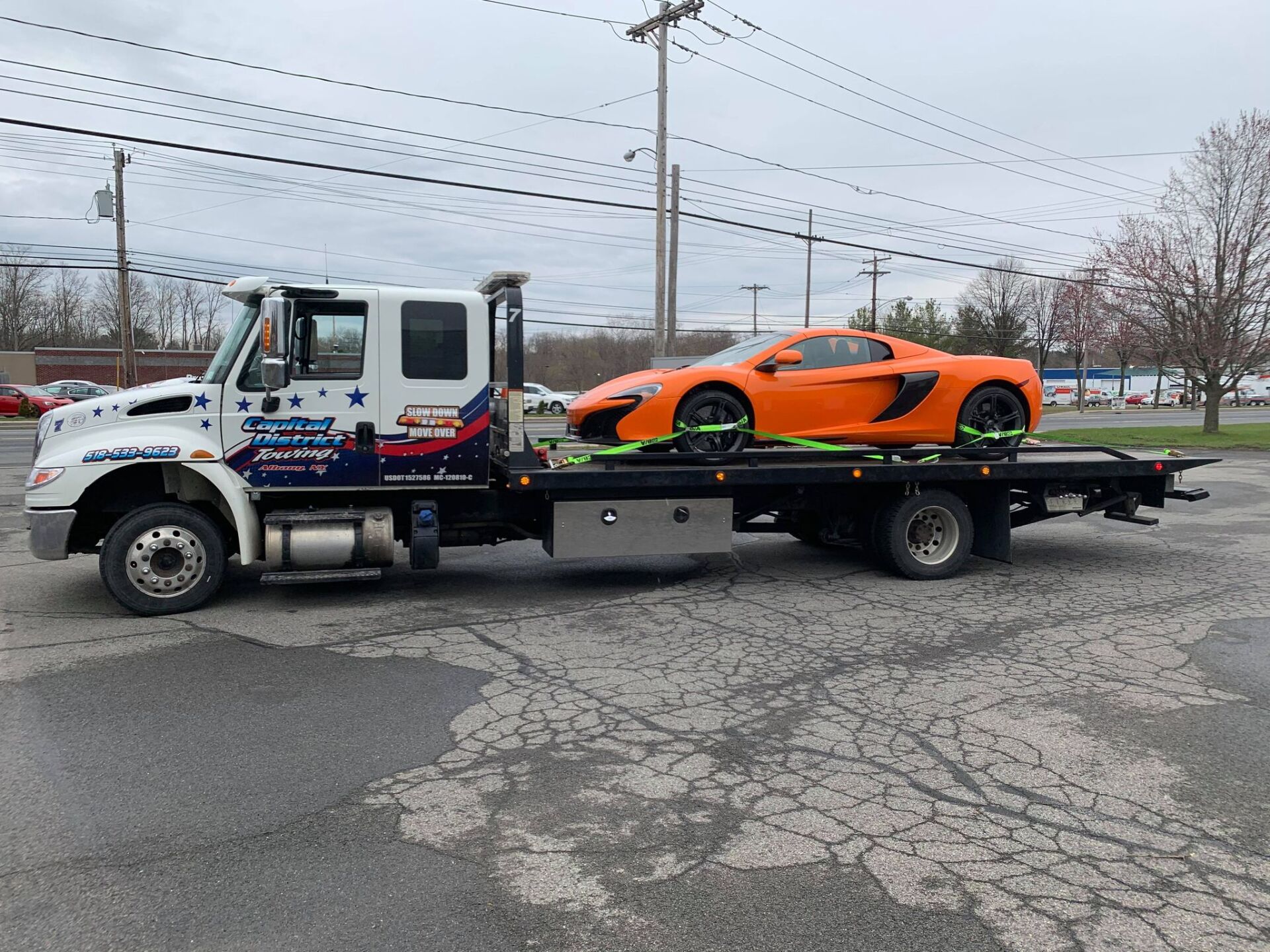 A tow truck is carrying a sports car on the back of it.