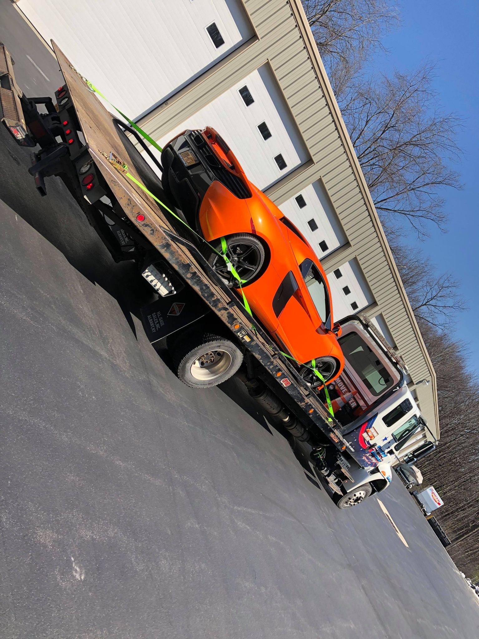 An orange car is being towed by a tow truck.