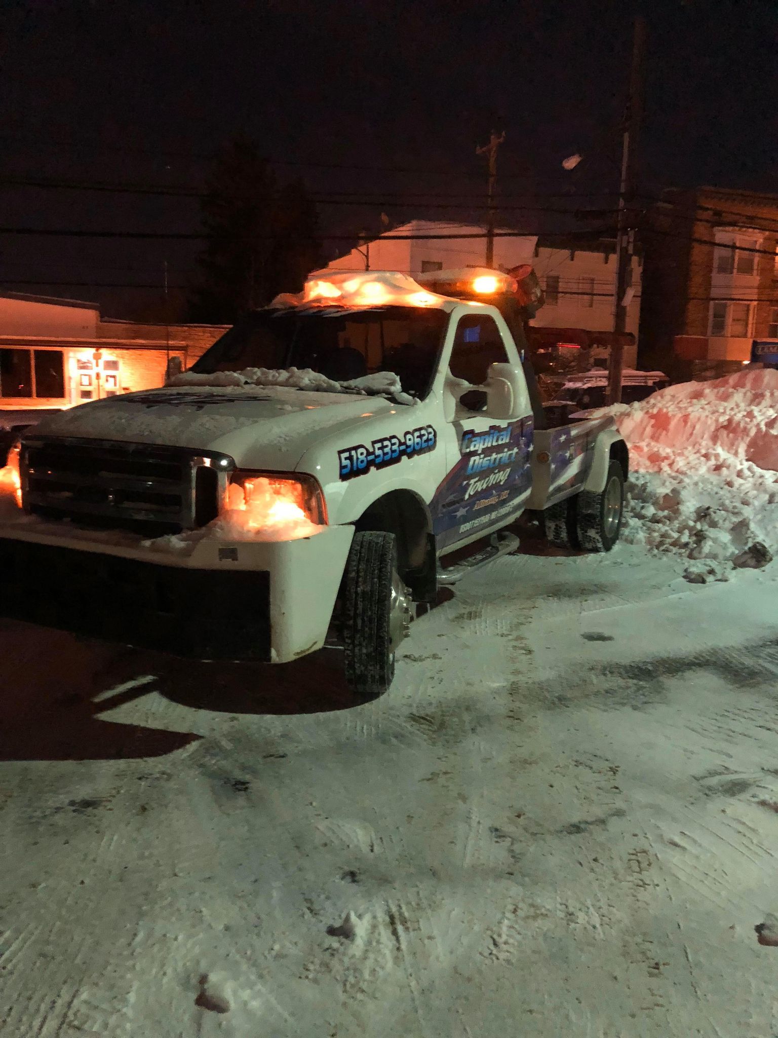 A white tow truck is parked in the snow at night.