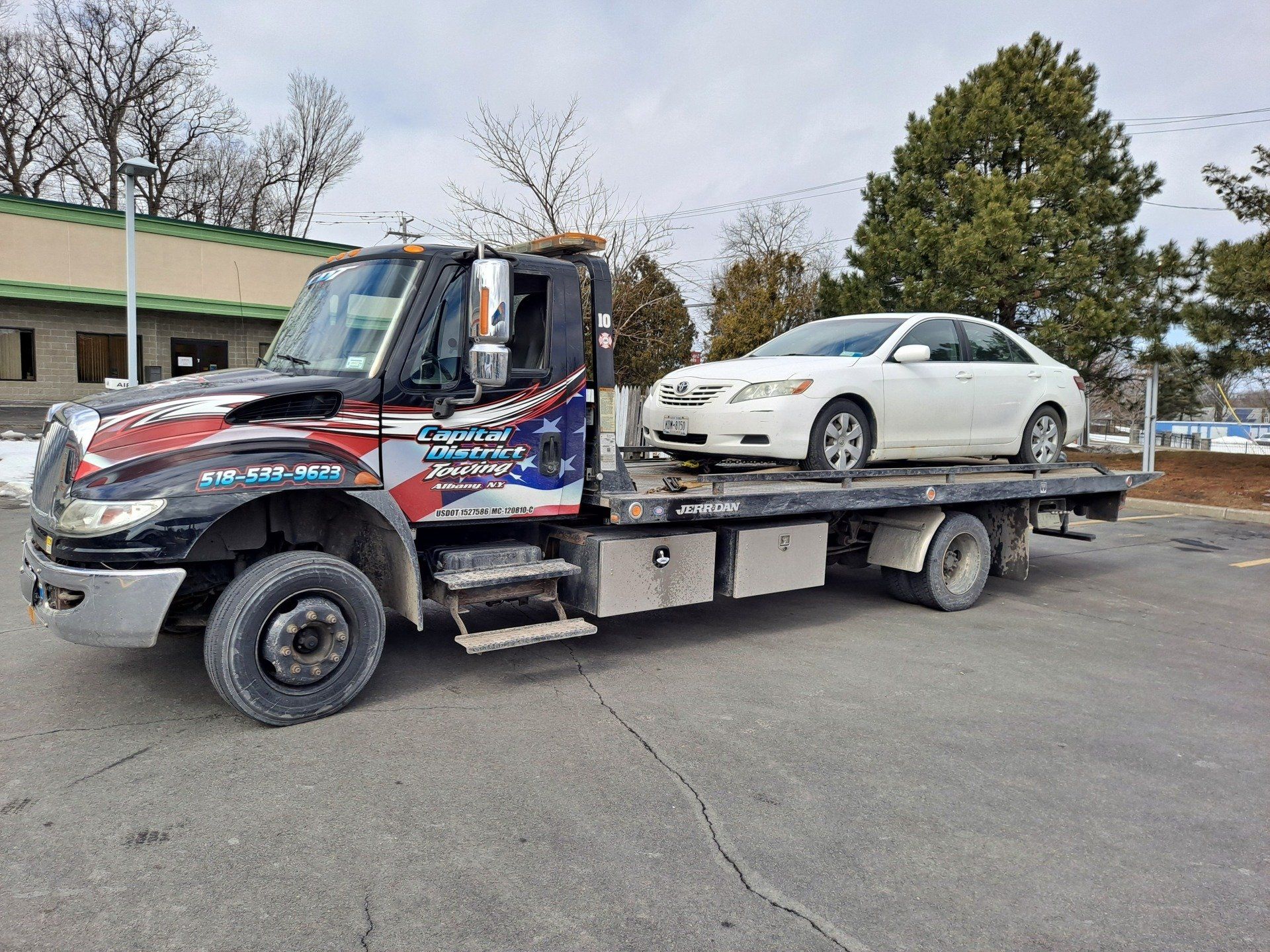 A tow truck with a car on the back is parked in a parking lot.