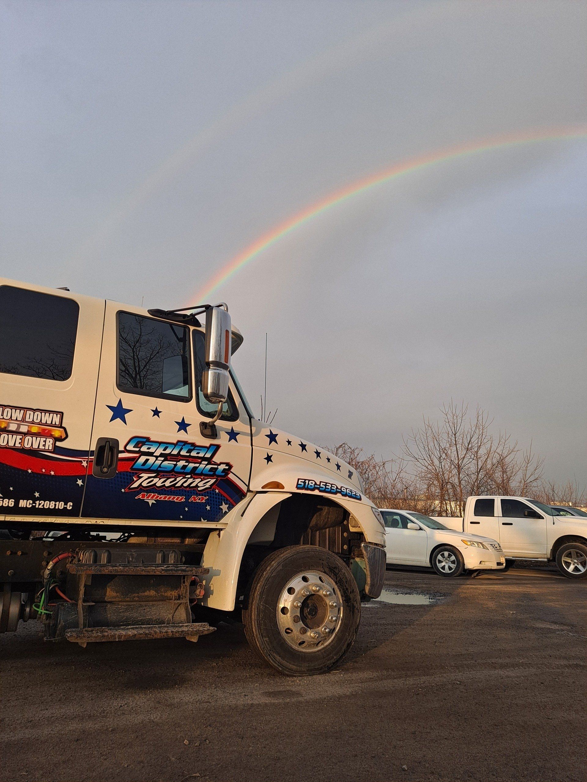 A truck is parked in a parking lot with a rainbow in the background