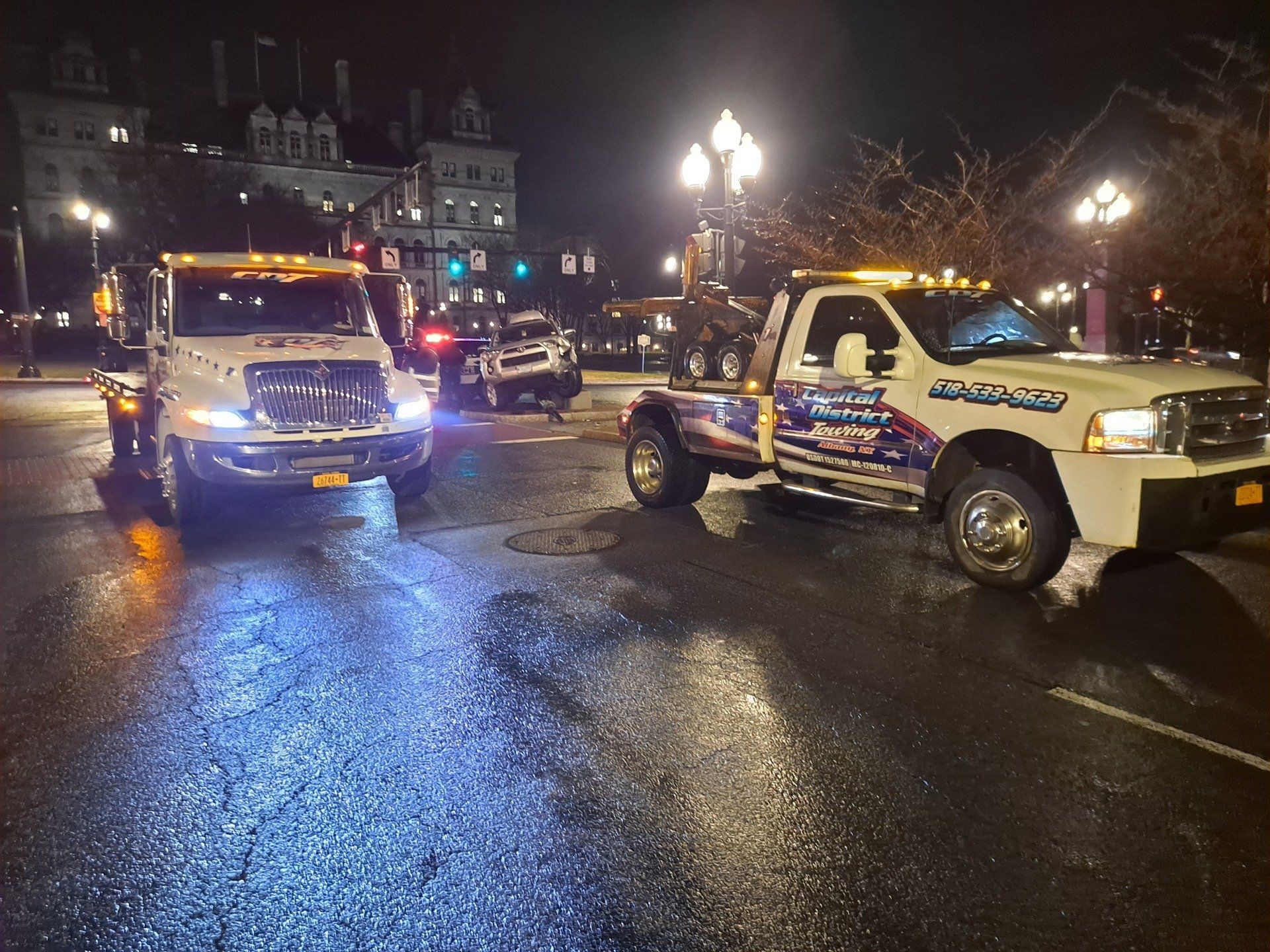Two tow trucks are parked on the street at night