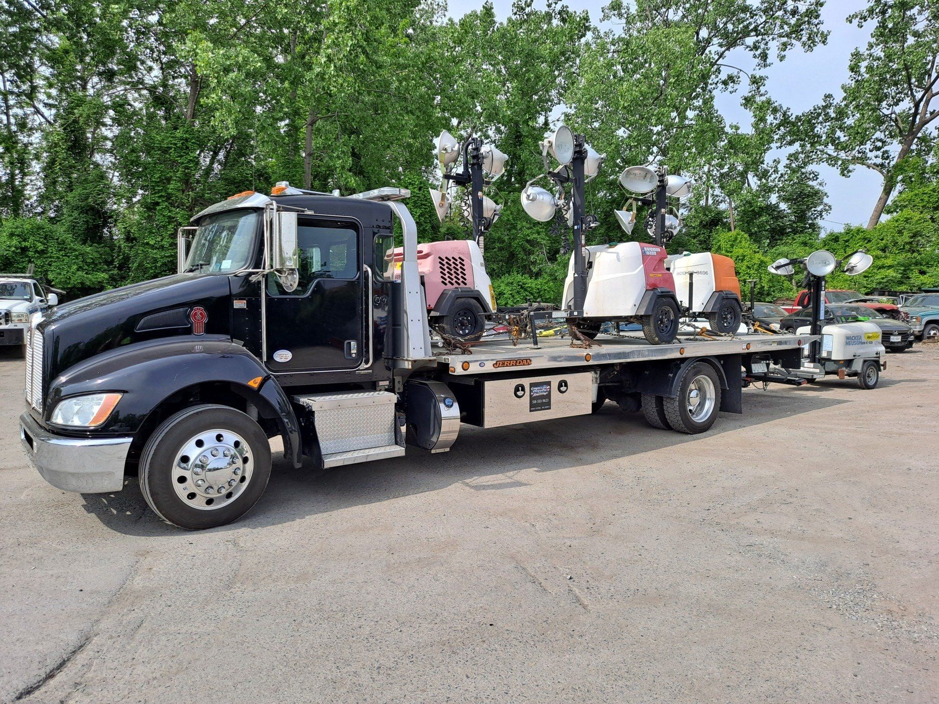 A black tow truck with a trailer is parked in a parking lot.