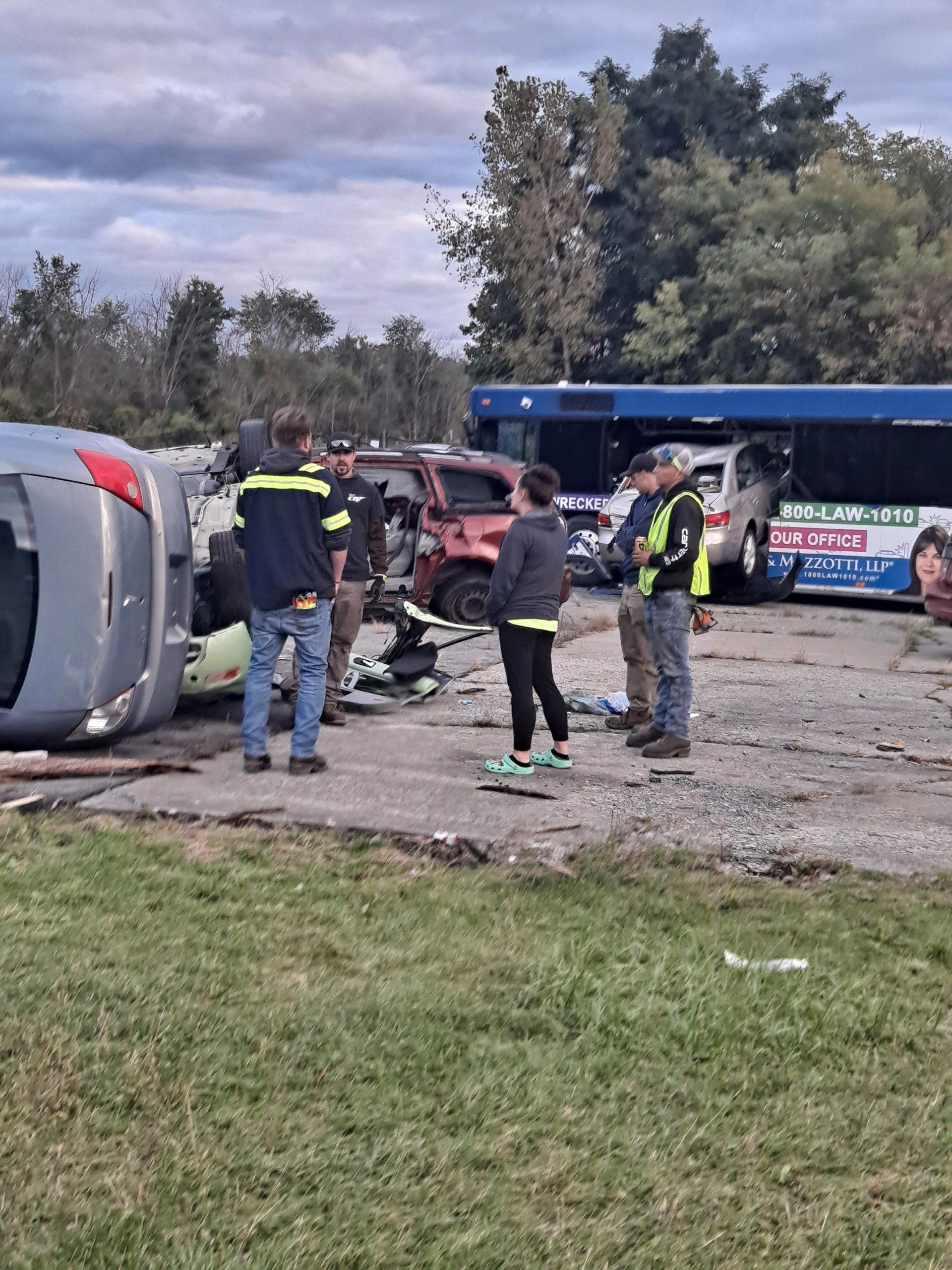 A group of people are standing around a car that has been flipped over.