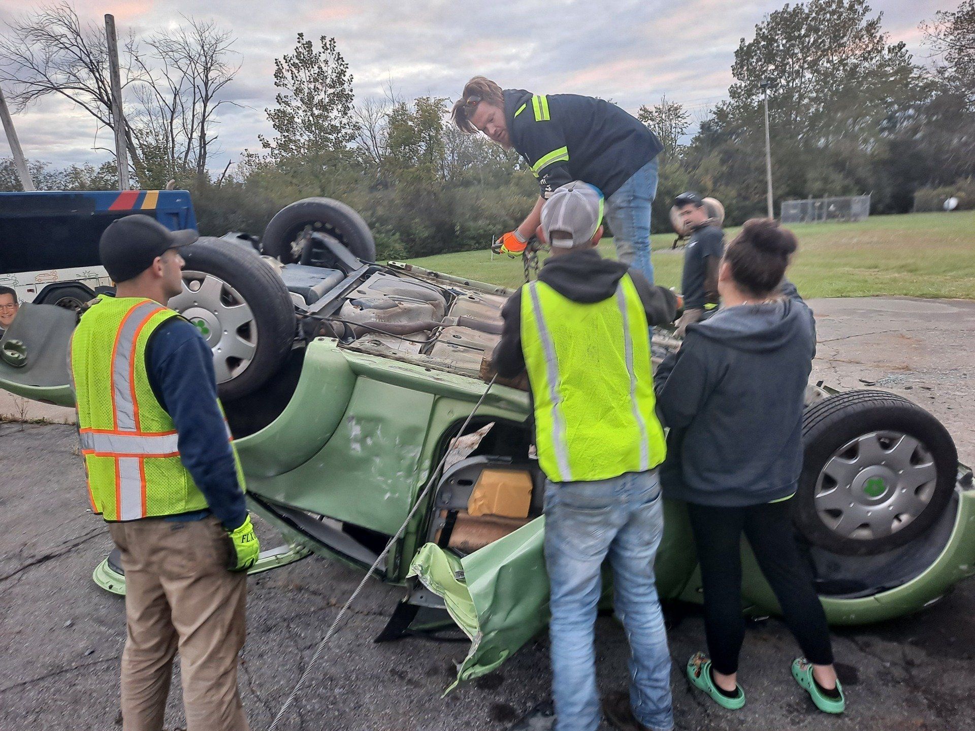 A group of people are working on a car that has fallen on its side.