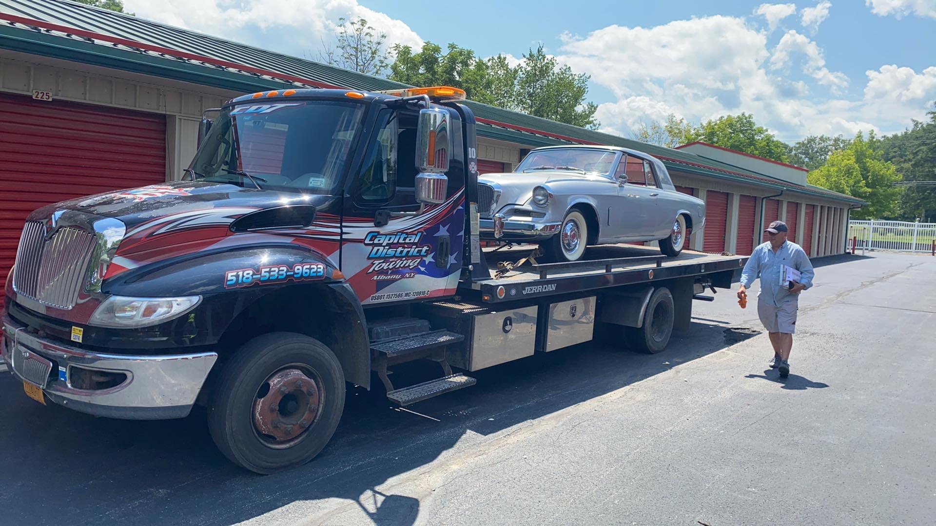 A man is standing next to a tow truck with a car on the back.