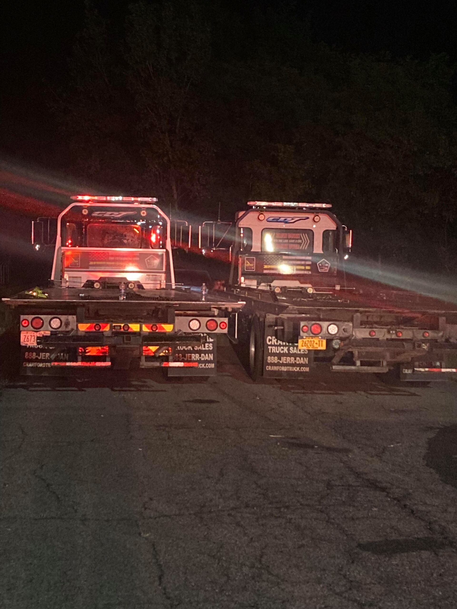 Two tow trucks are parked on the side of the road at night