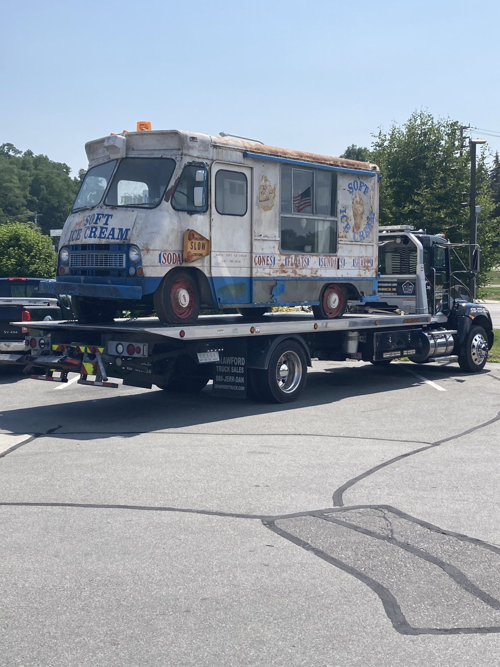 An ice cream truck is being towed by a tow truck.