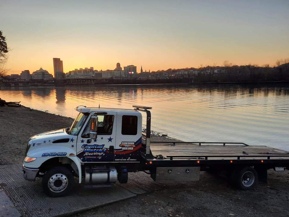 A tow truck is parked on the shore of a body of water.