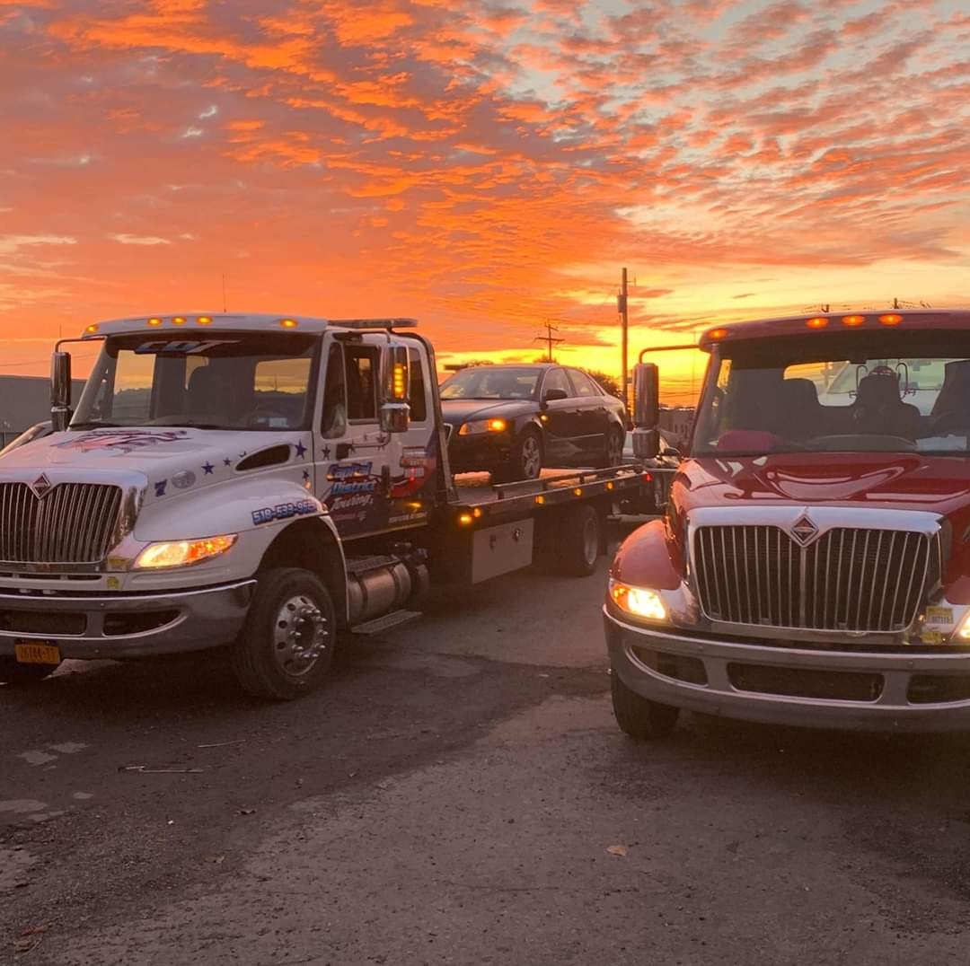 Two tow trucks are towing a car down a road at sunset.