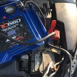 A blue jump starter is sitting under the hood of a car.