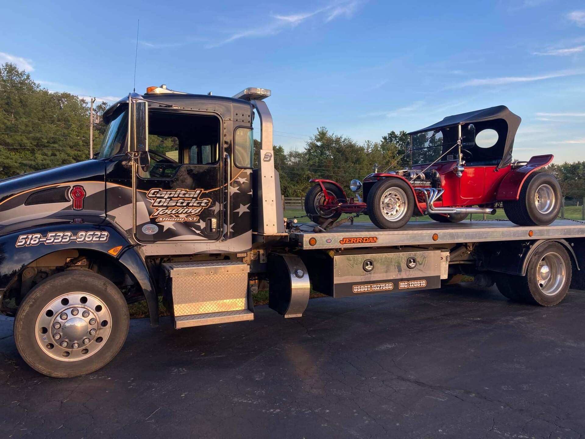 A tow truck is carrying a red buggy on the back of it.