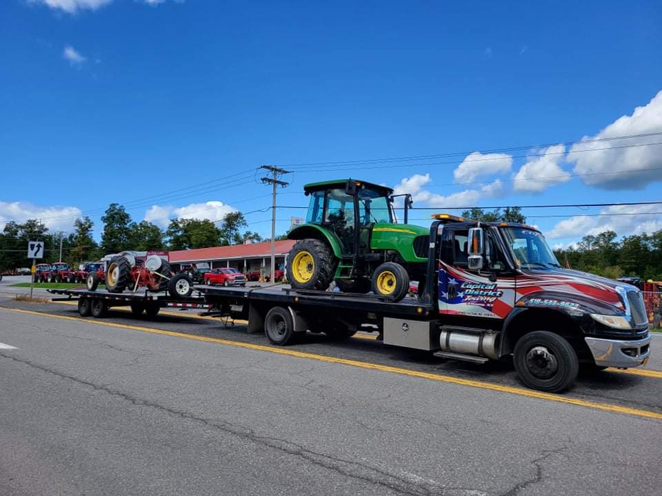 A tow truck is carrying a green john deere tractor on a trailer.