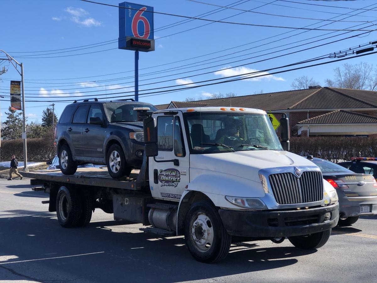 A tow truck with a car on the back is parked in front of a motel 6 sign.