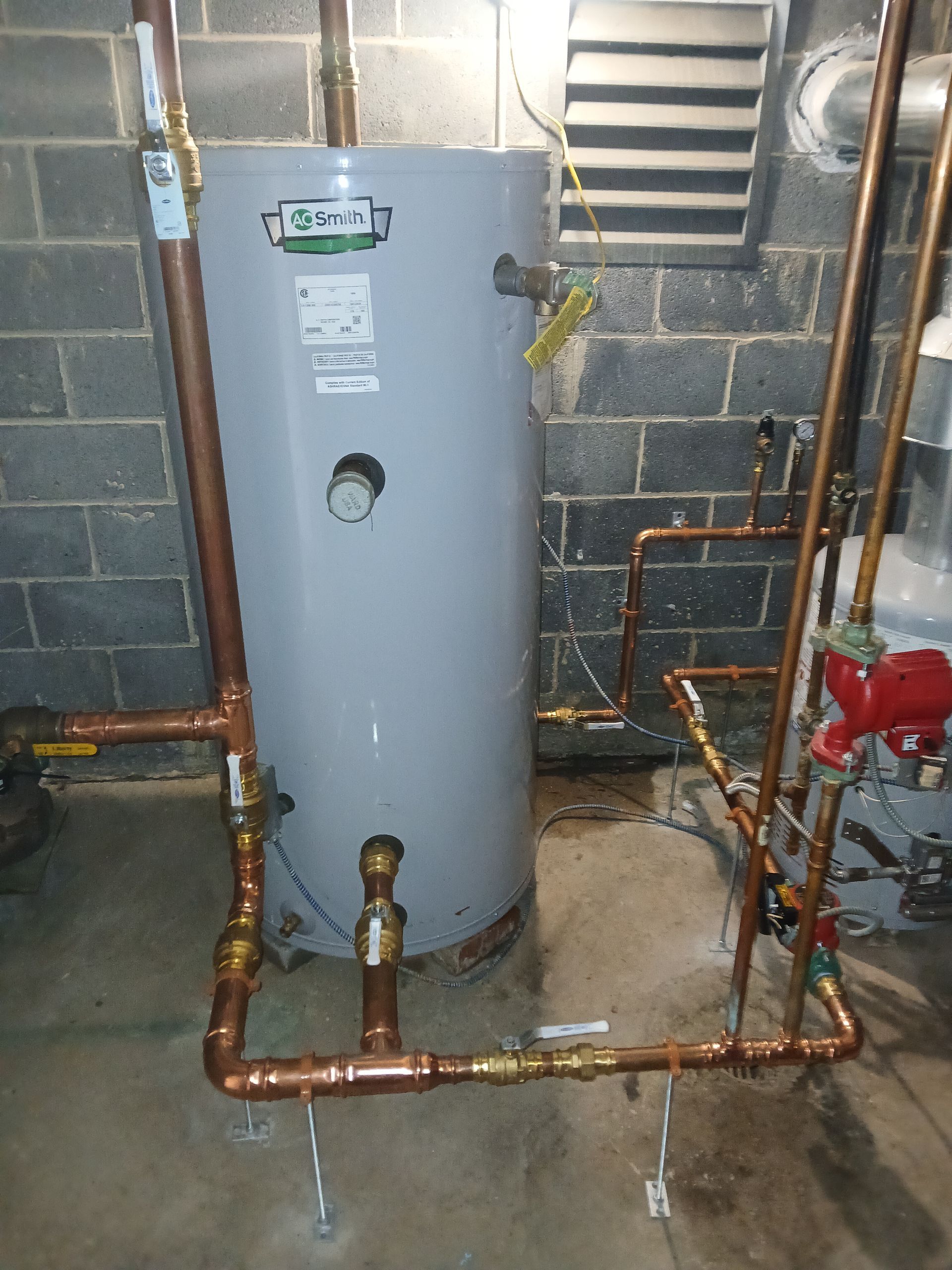 Basement utility room with a gray water heater, copper pipes, and cinder block walls.
