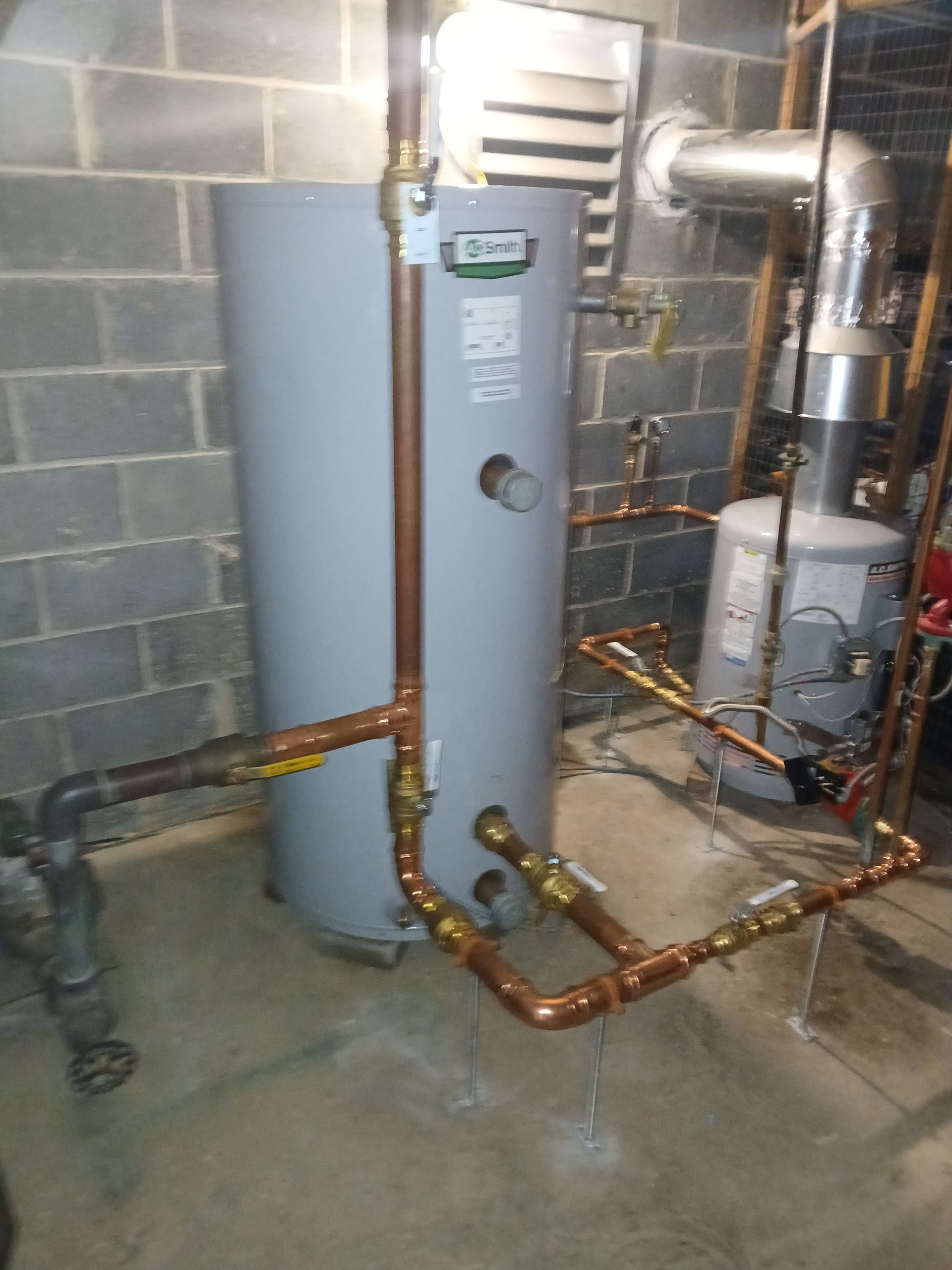 Basement utility room with a gray water heater, copper piping, and HVAC equipment against cinderblock walls