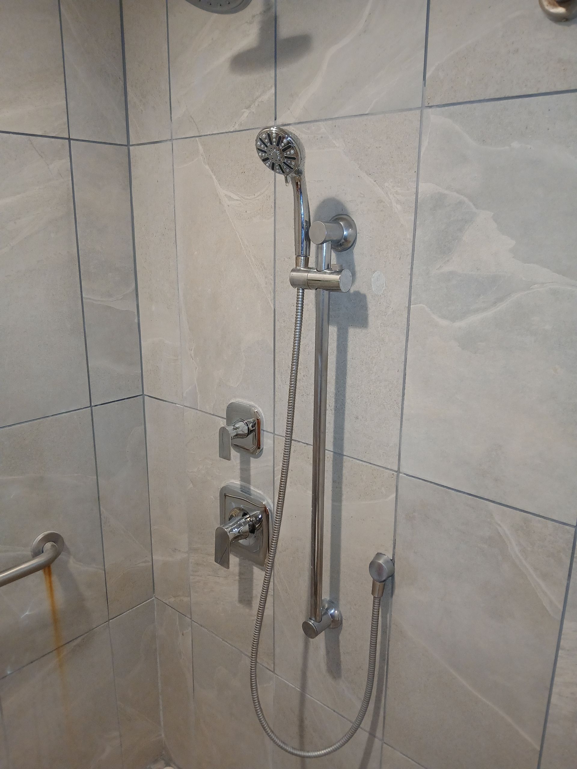 Bathroom shower with tiled wall, handheld showerhead, and control valves.