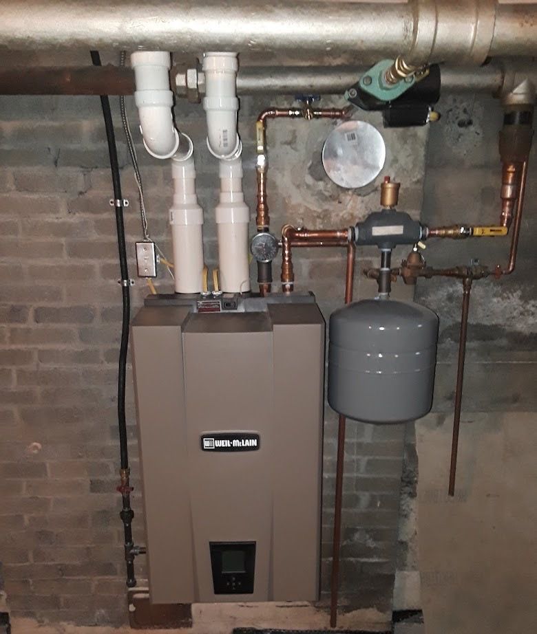Boiler room with wall-mounted water heater, copper pipes, and gray expansion tank against a brick wall