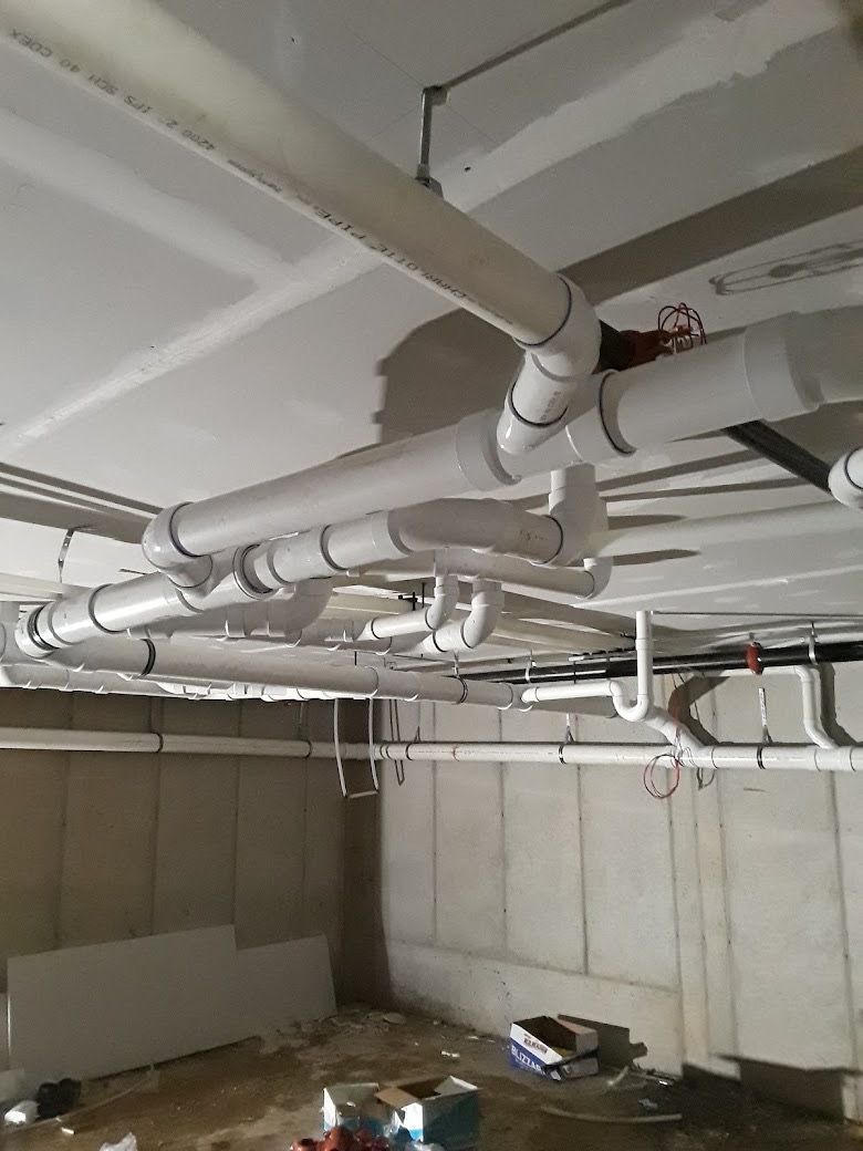 Basement ceiling with white pipes and ductwork above concrete block walls