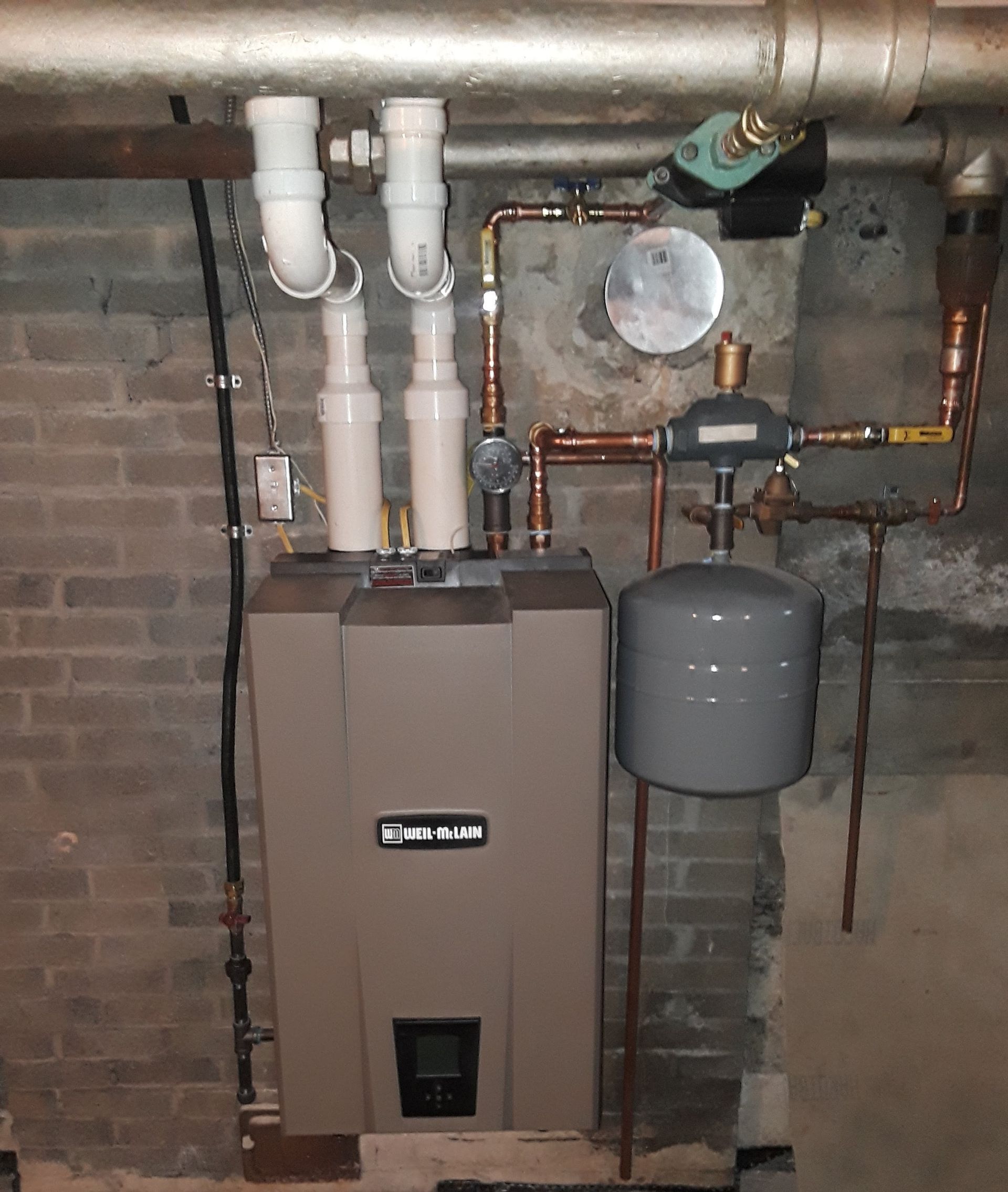 Basement utility room with furnace, water heater, pipes, and gray expansion tank against brick wall