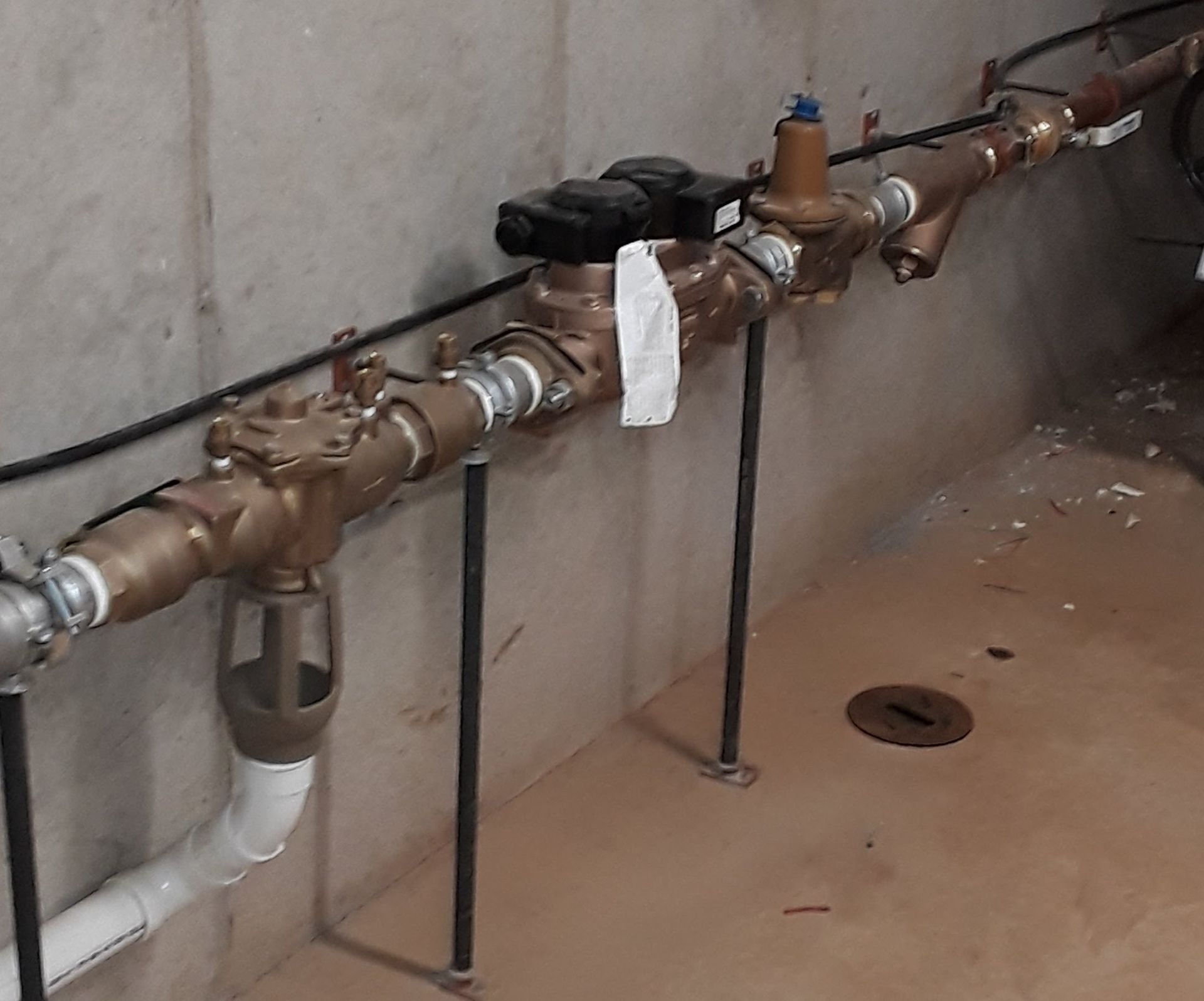 Valves and pipes mounted along a wall, with a small white cloth hanging from one pipe.