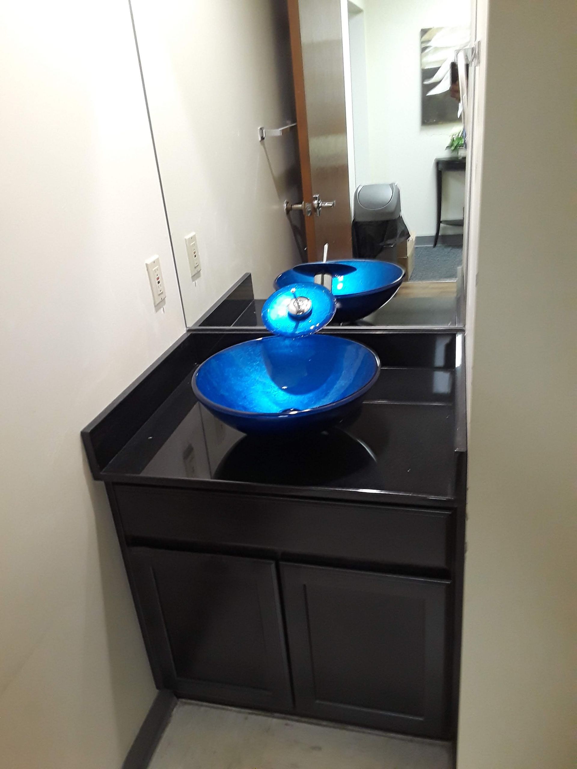 Black bathroom vanity with blue glass vessel sinks and mirror in a narrow hallway