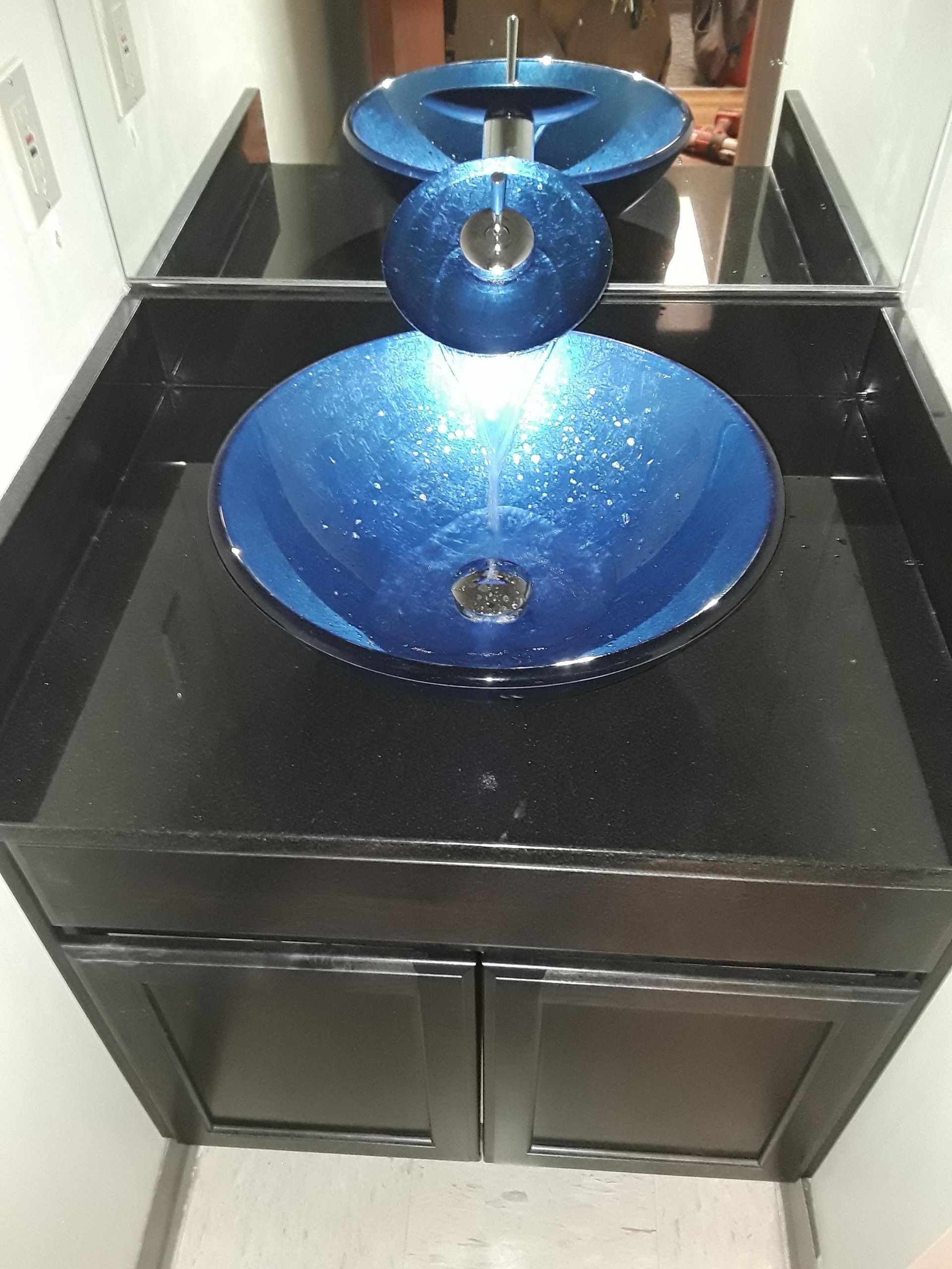 Blue glass vessel sink on a black vanity in a bathroom with a mirror behind it
