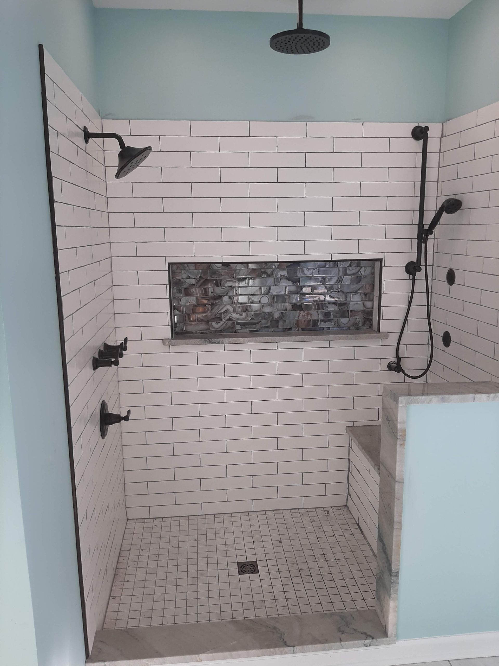 Empty tiled shower stall with white subway tiles, mosaic floor, and teal walls.