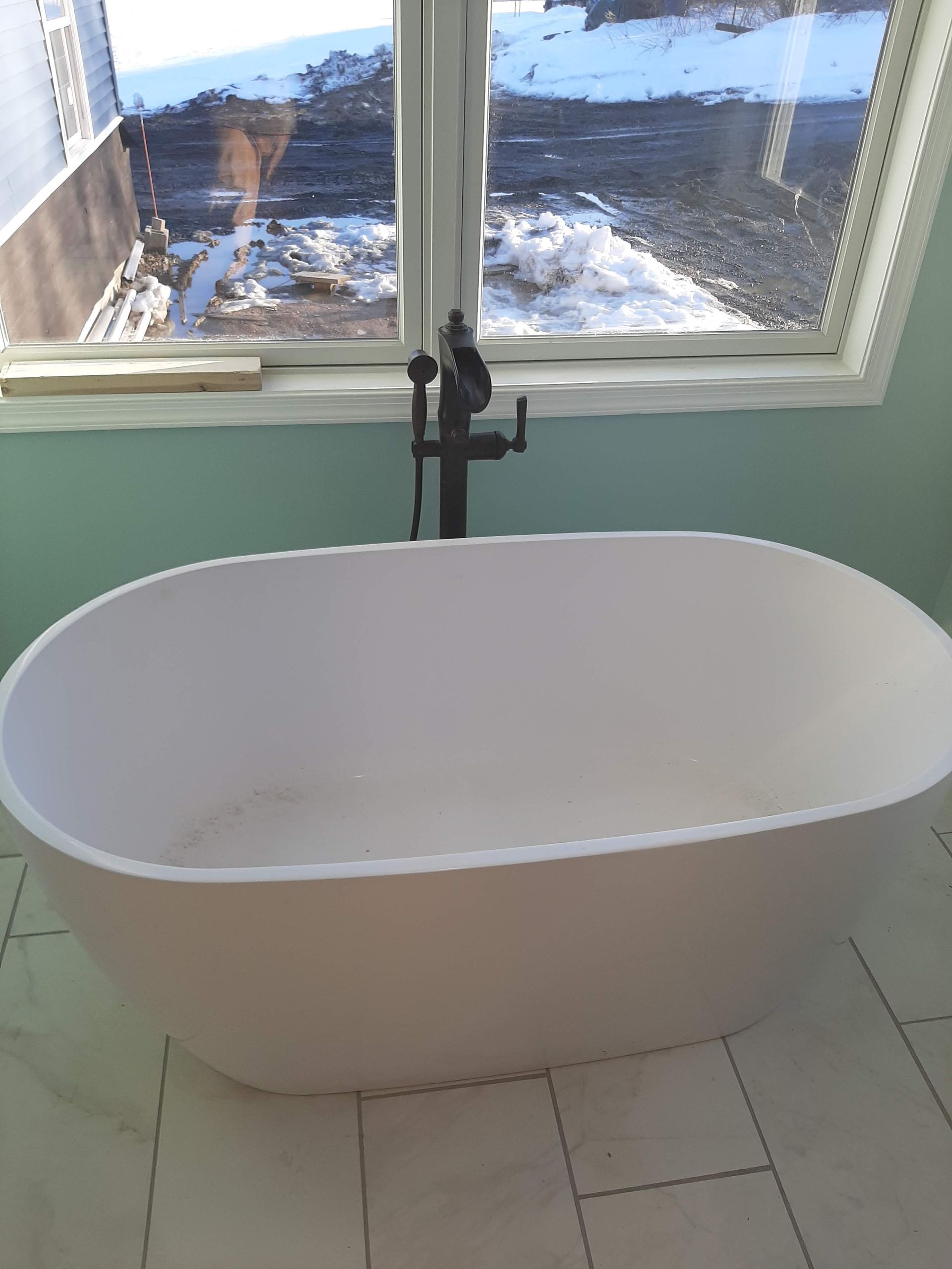 White freestanding bathtub in a tiled room beneath a window