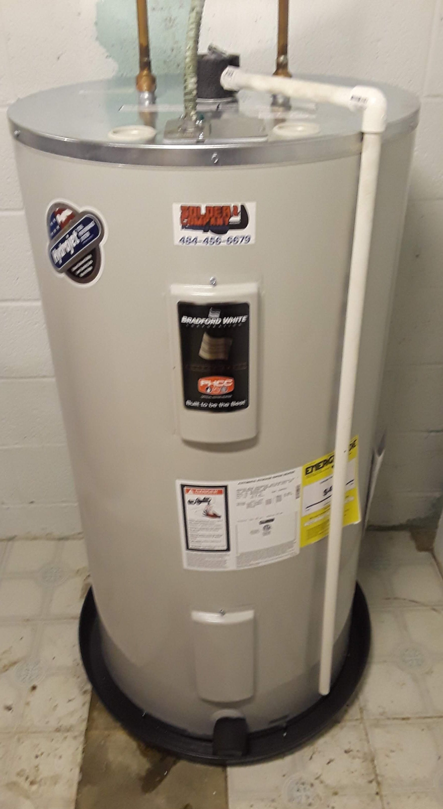 Gray water heater with visible pipes and labels in a basement or utility room