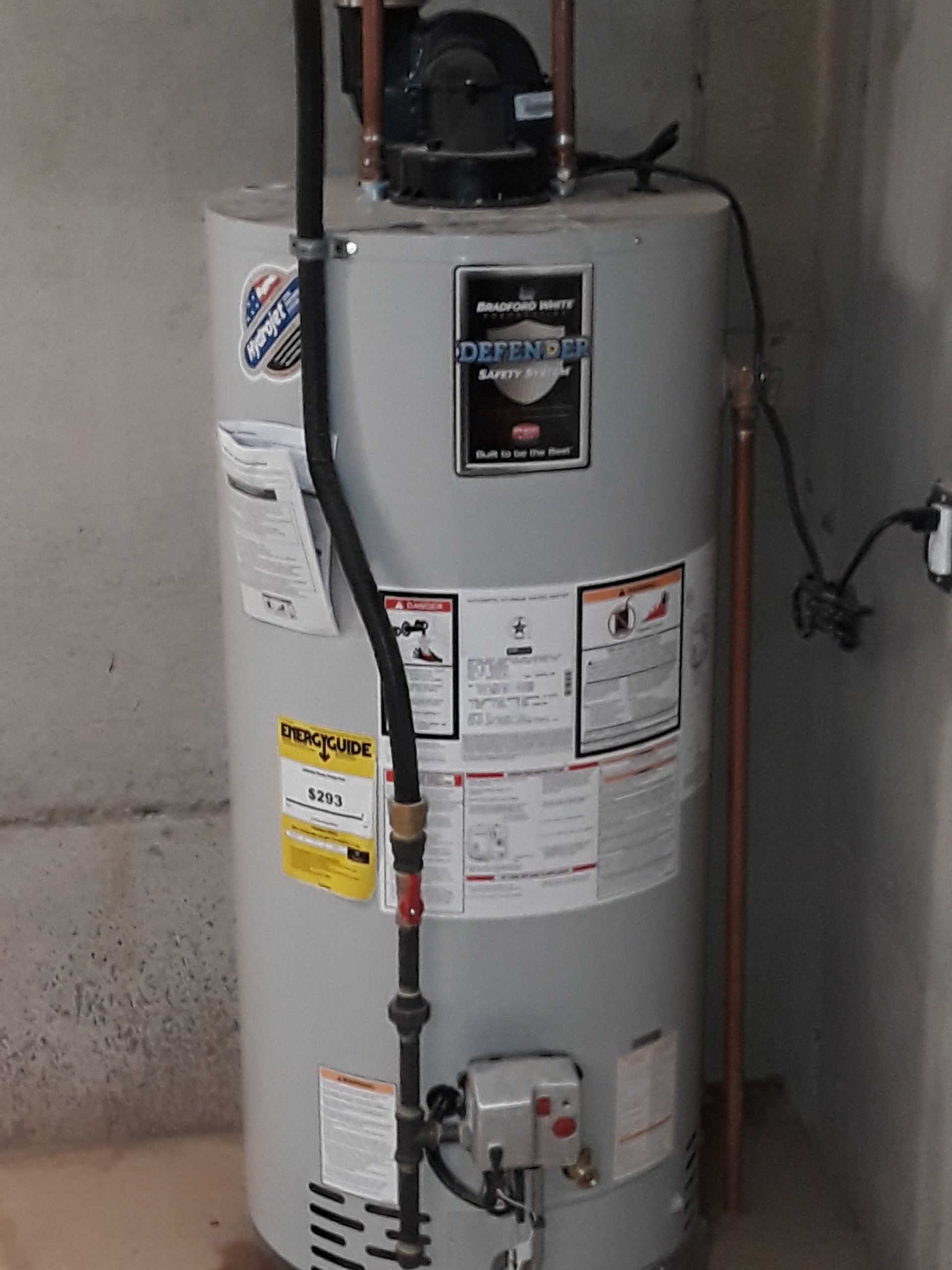 Gray water heater in a utility room with pipes and warning labels