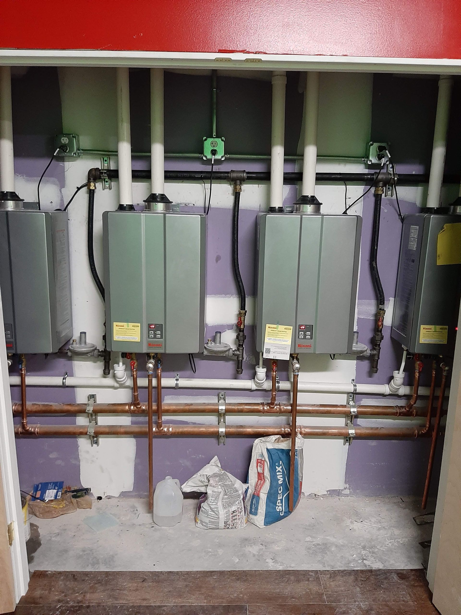 Three gray water heaters with copper pipes in a utility closet