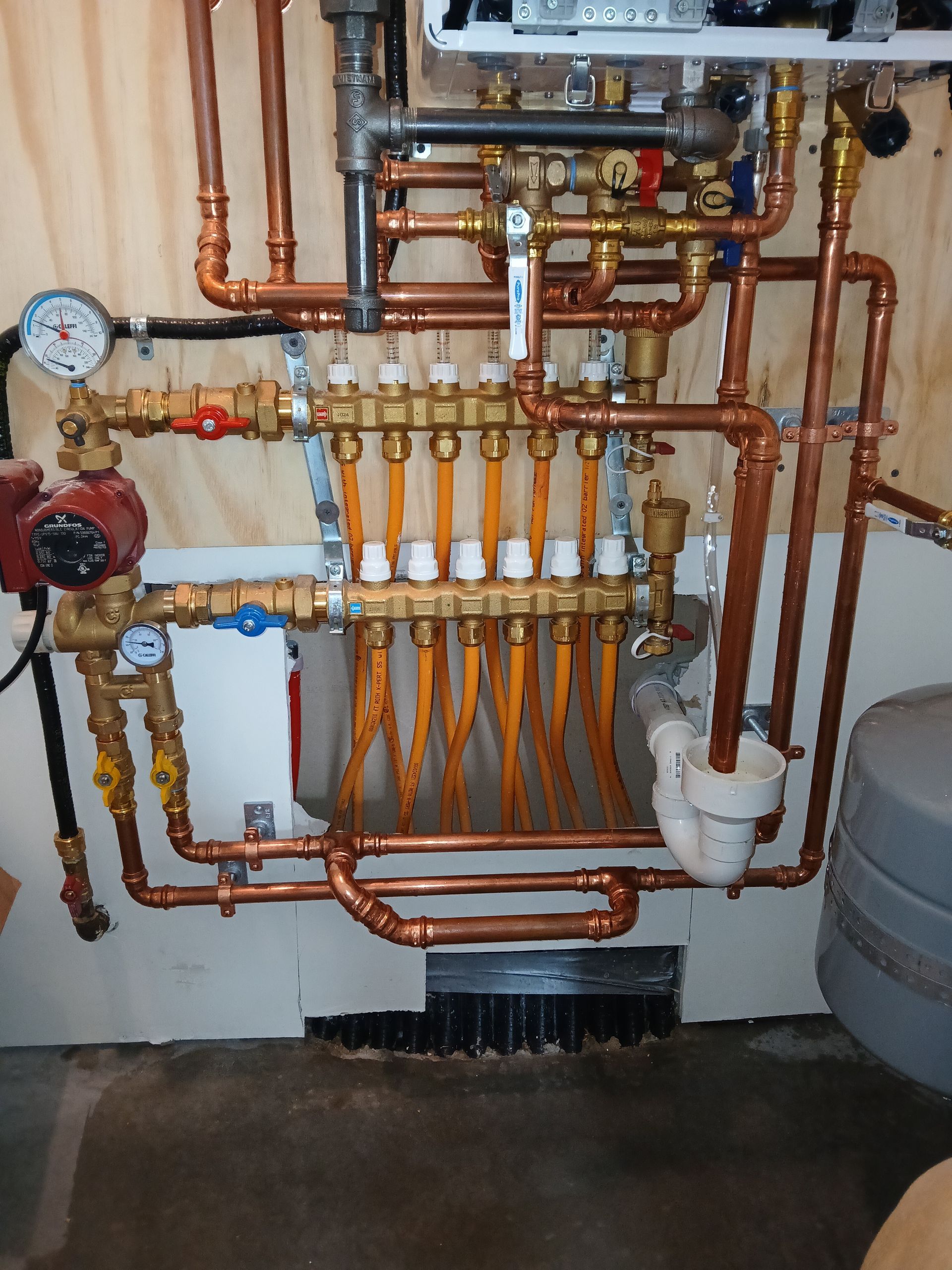 Copper plumbing manifold with gauges and valves mounted on a wall in a utility room