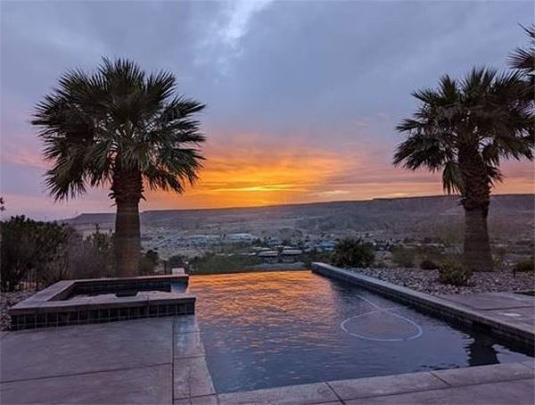 A sunset over a swimming pool with palm trees in the foreground