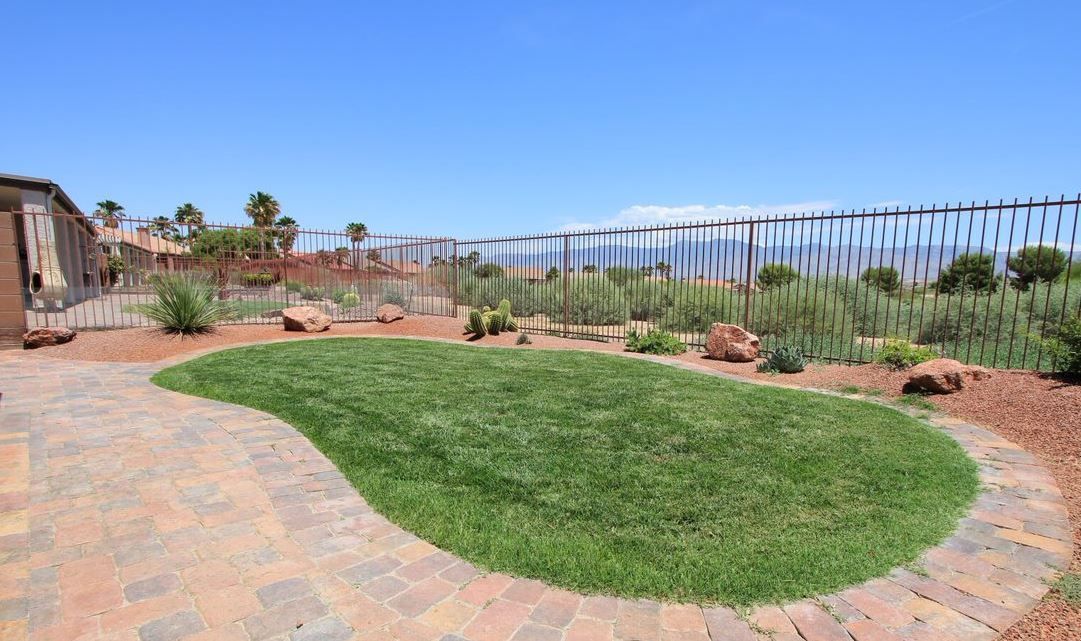 A lush green lawn with a brick walkway and a fence in the background.