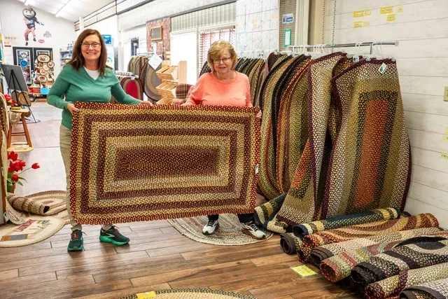 Two women are holding a rug in a store.