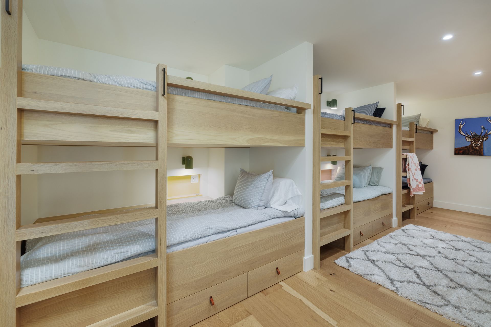 Bright bedroom with wooden bunk beds, white bedding, a rug, and a person standing near the back wall