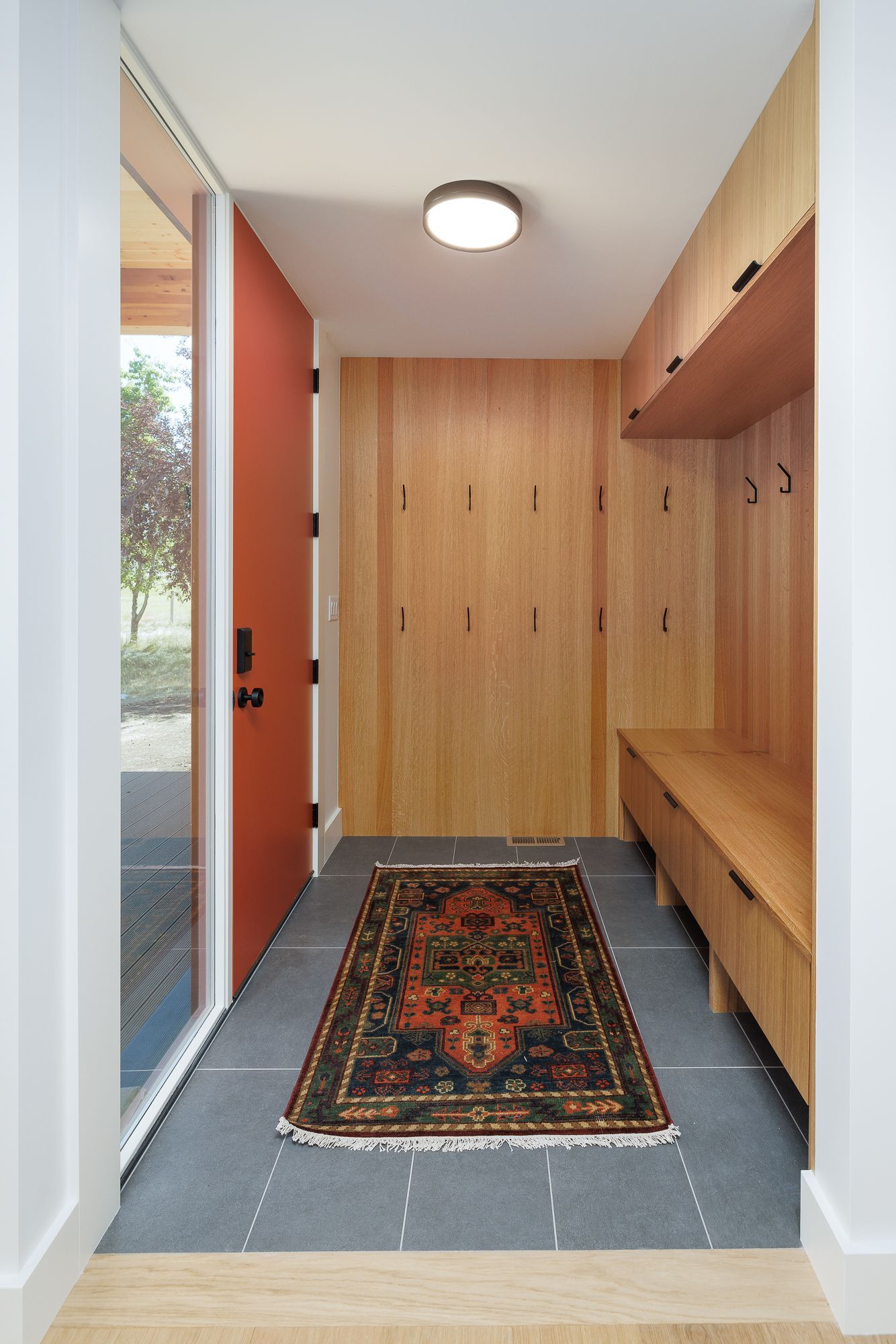 Modern entryway with wood built-ins, orange door, gray tile floor, and patterned rug