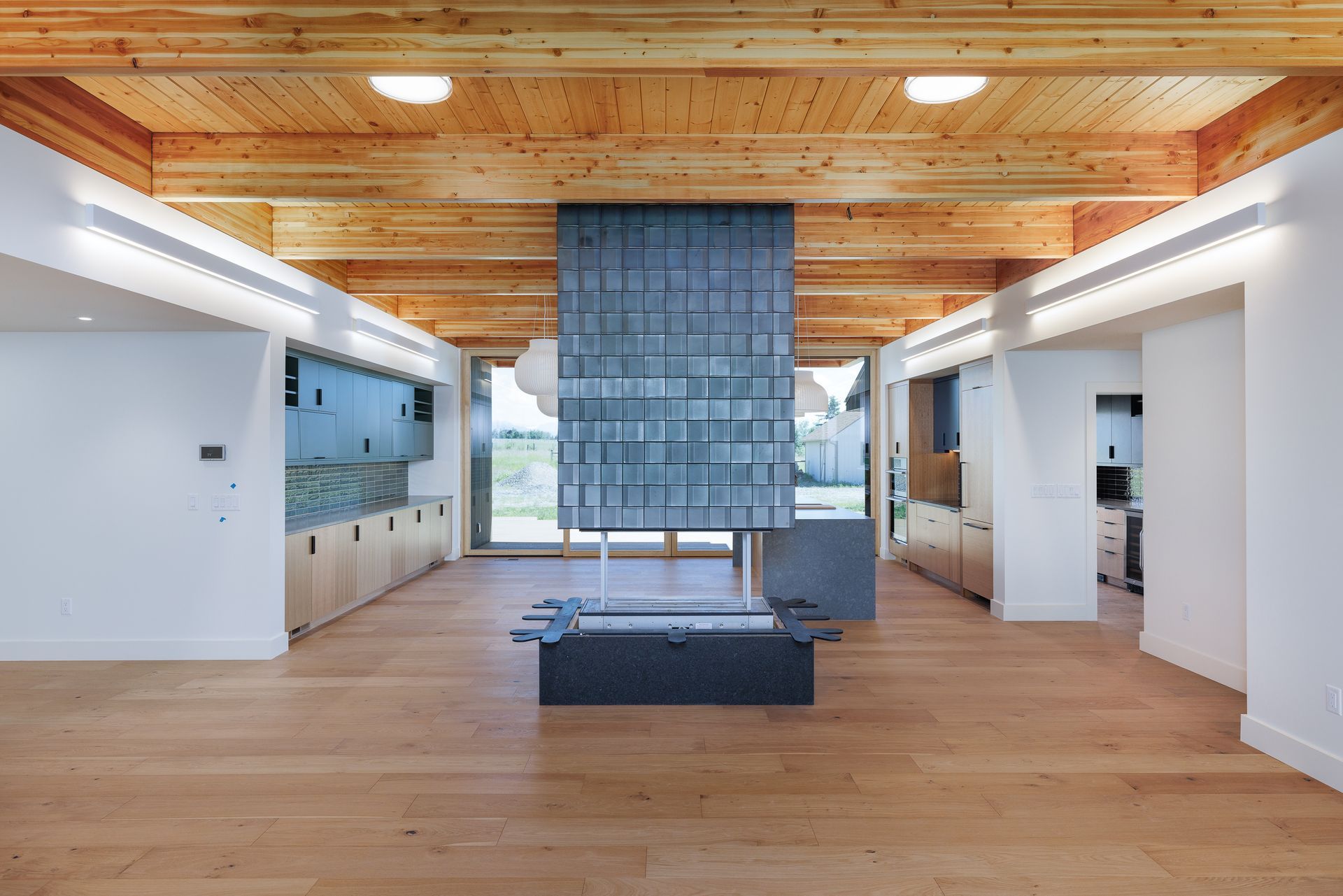 Modern open-plan living room with wood ceiling, white walls, and a large blue window shade.