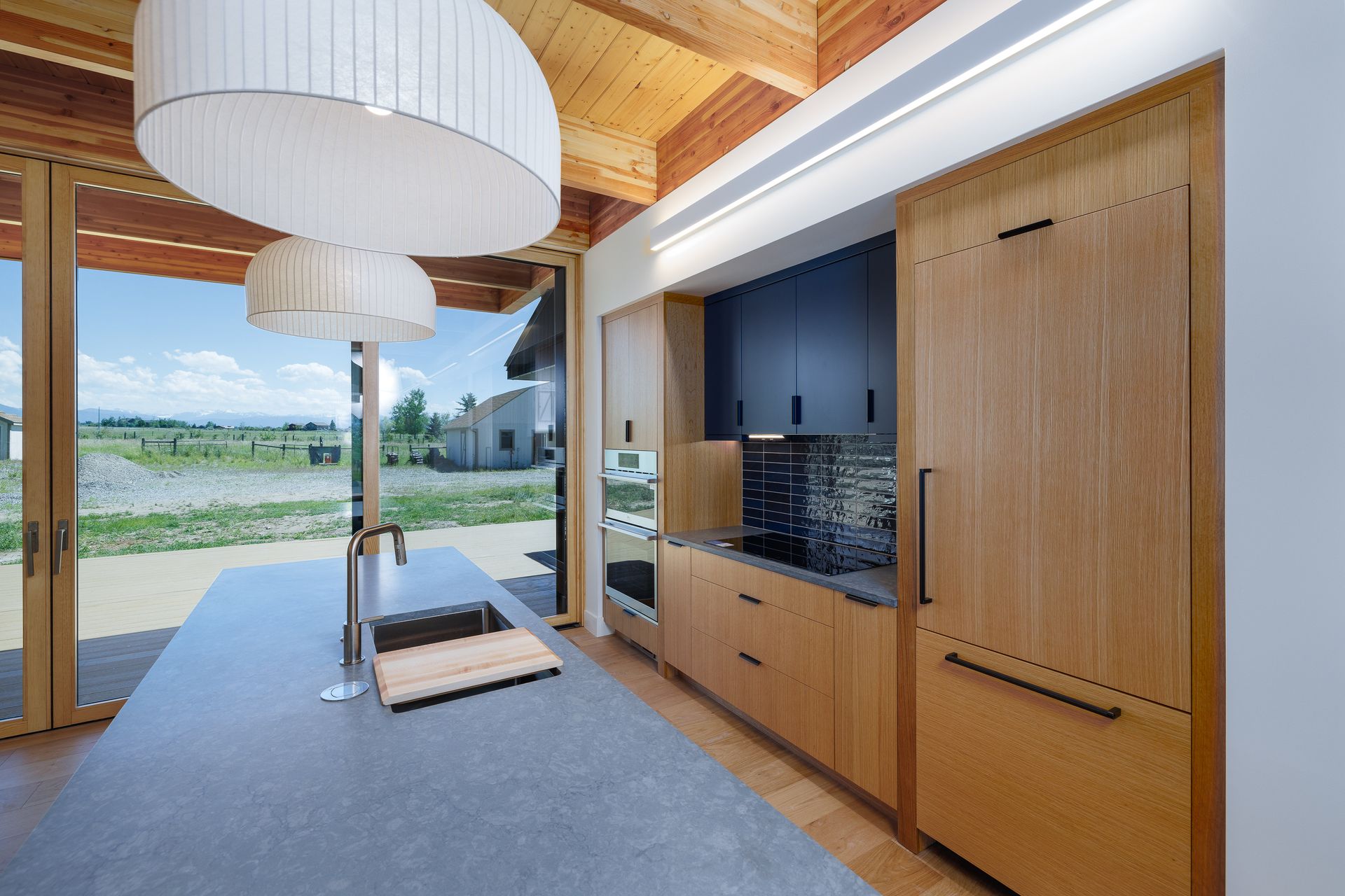 Modern wood-and-glass room with large windows, pendant lights, built-in cabinetry, and a view of the landscape outside