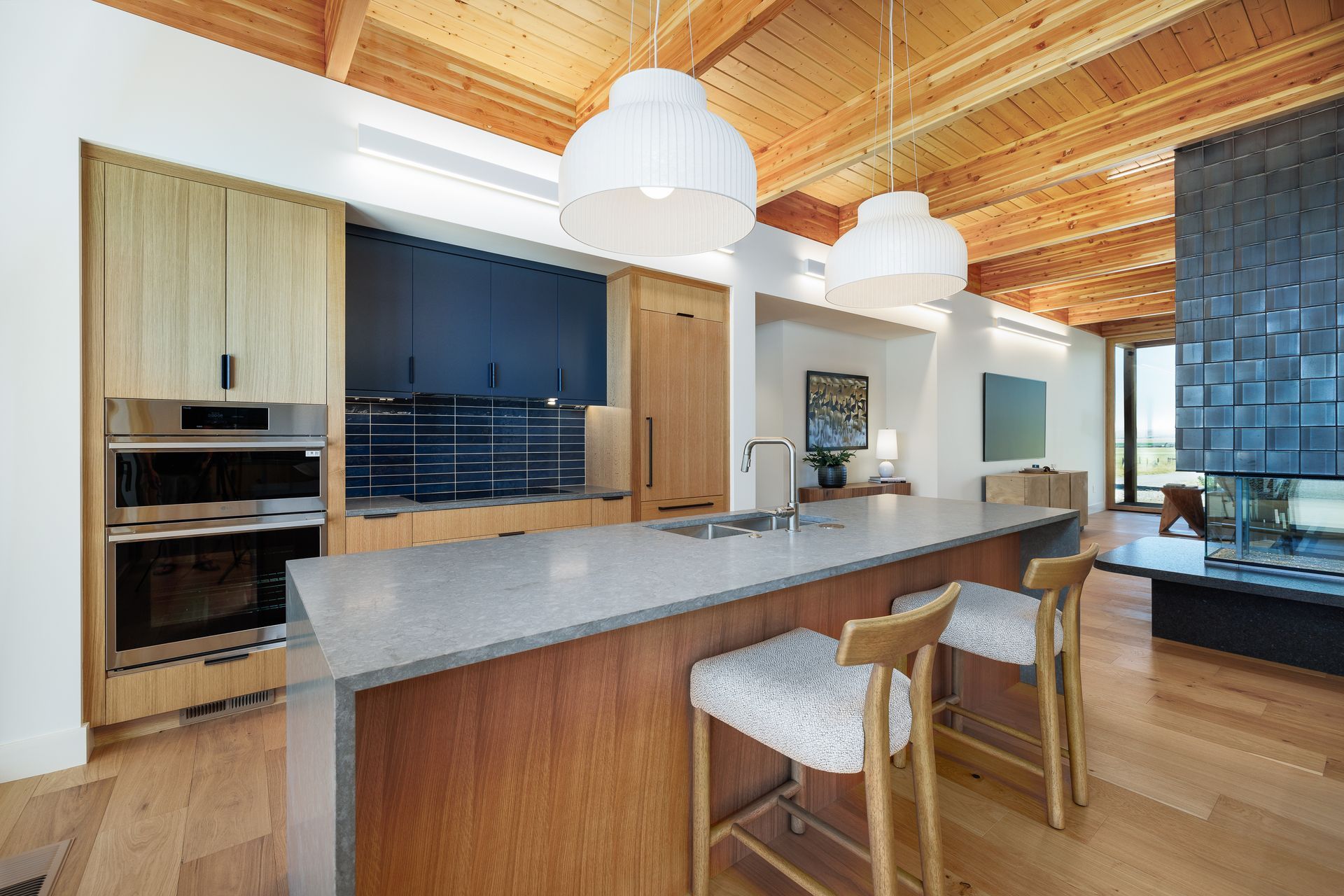 Modern kitchen with wood cabinetry, large island, pendant lights, and blue tile backsplash