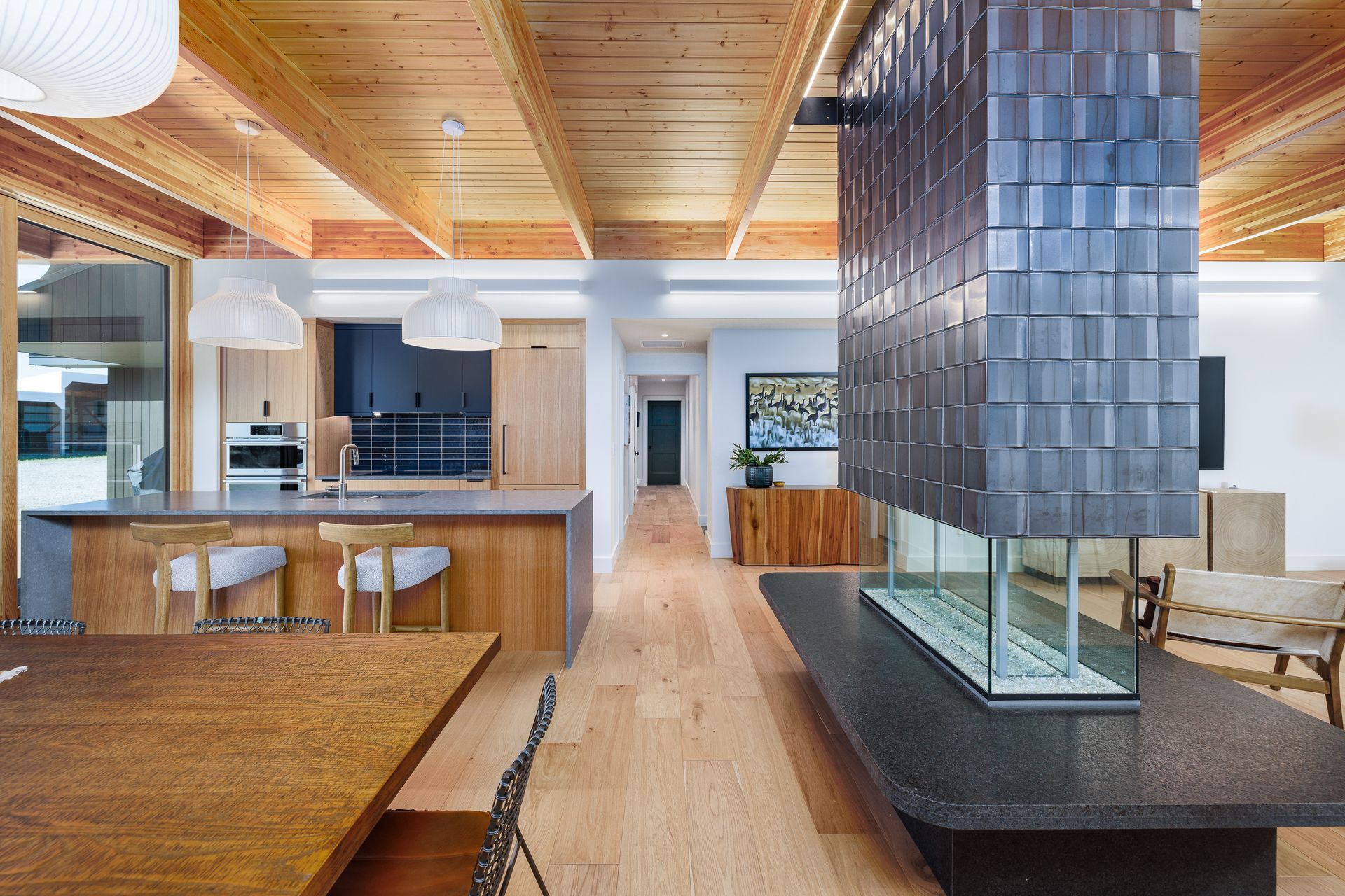 Modern open-concept kitchen and dining area with wood ceiling, island seating, and central tiled column.