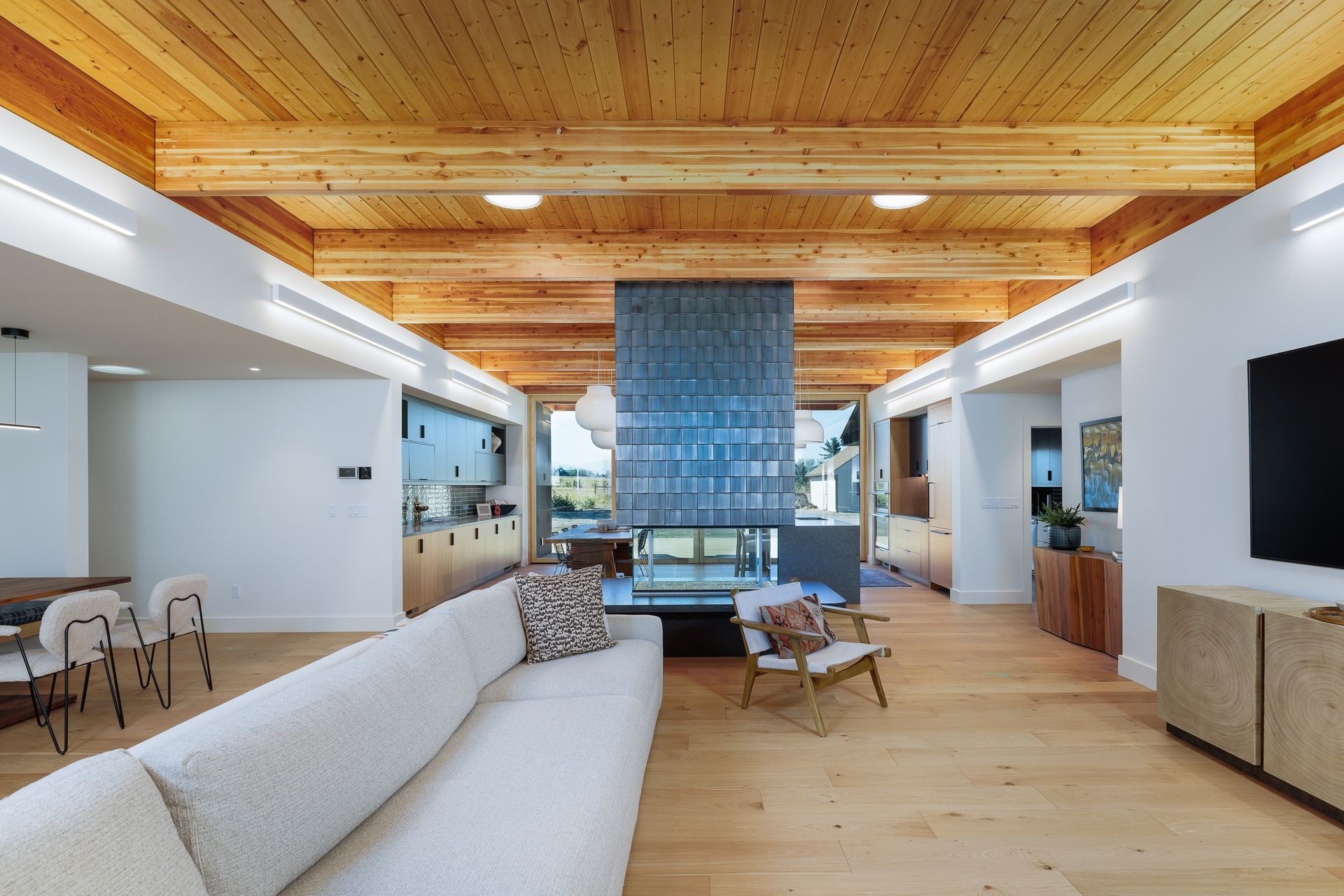 Modern living room with wood ceiling, blue curtains, sofa, chairs, and large TV amid open white walls