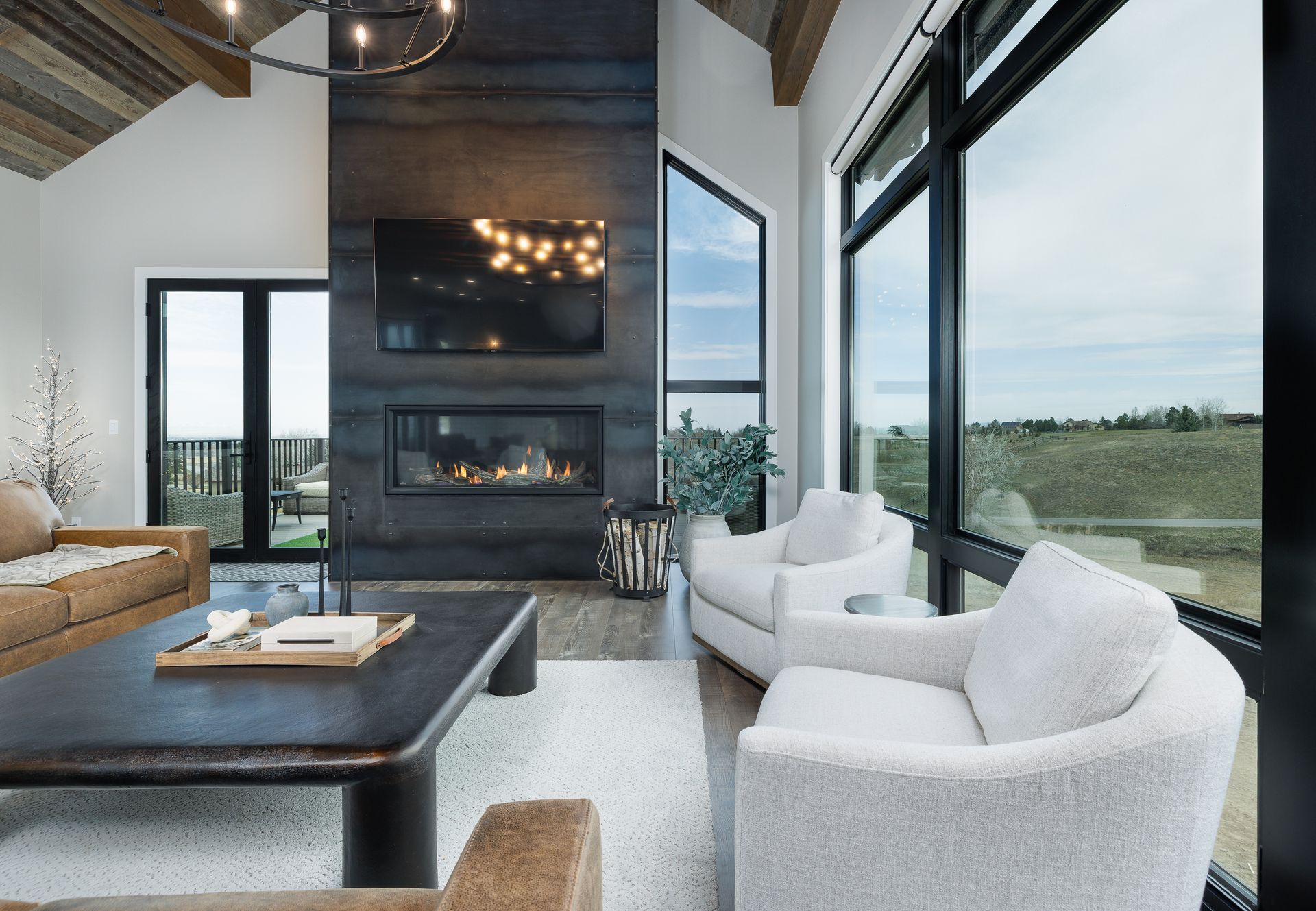 Modern living room with fireplace, sectional sofa, white chairs, and large windows overlooking a field
